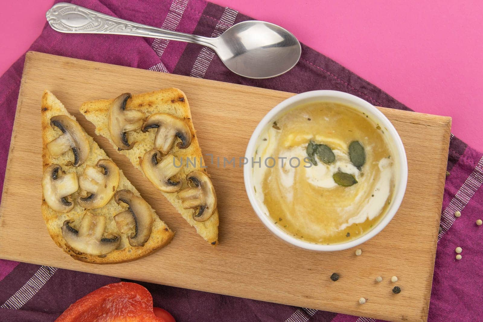Pea soup with croutons stands on a green towel, next to there are tomatoes, toasts of pumpkin seeds, everything stands on the yellow table.