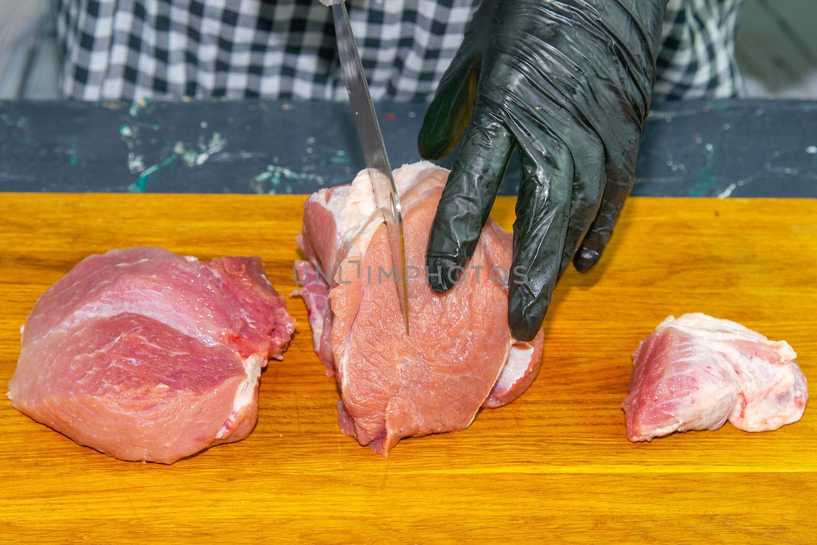 Female hands in black gloves cut juicy slices of pork, garlic stands nearby.
