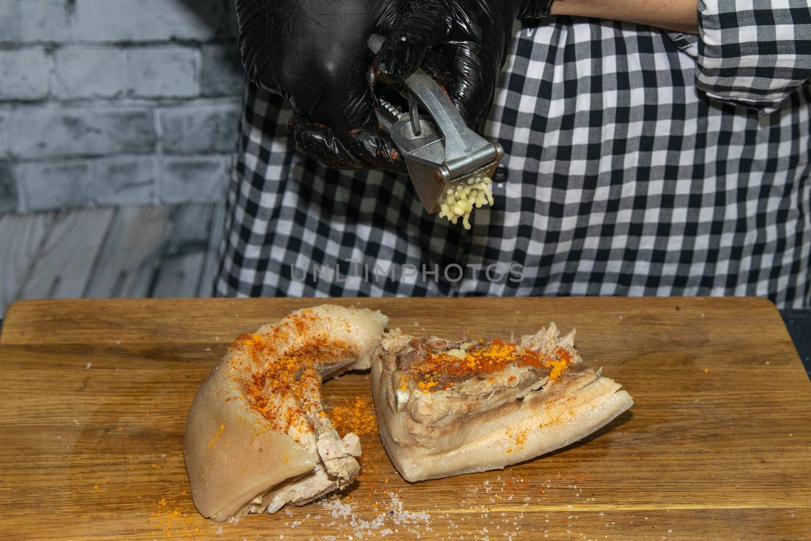 Female hands in black gloves cut juicy slices of pork, garlic stands nearby.