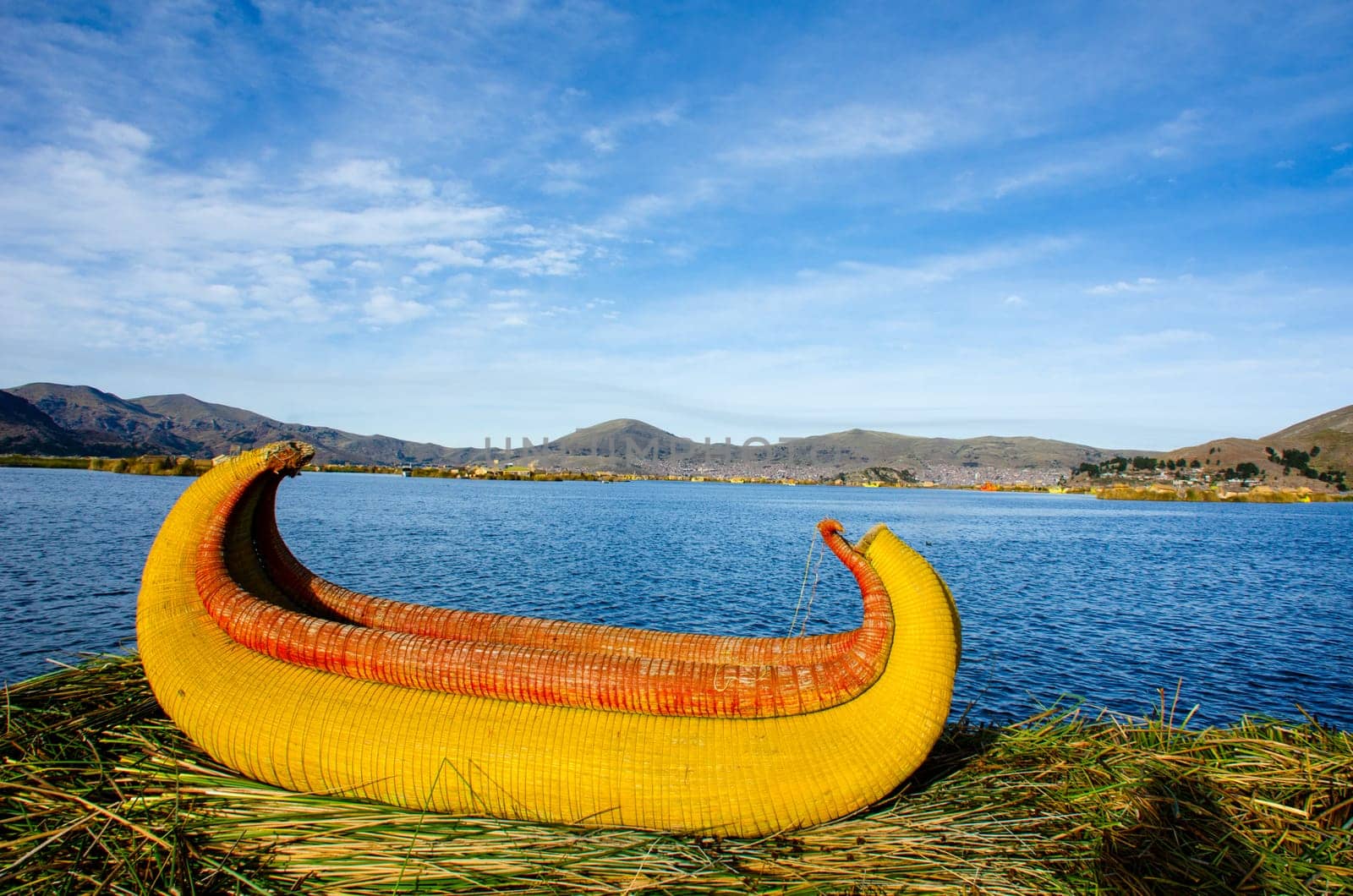 A reed canoe on the banks of the Uros Islands at Lake Titicaca. Puno, Peru on the far bank.