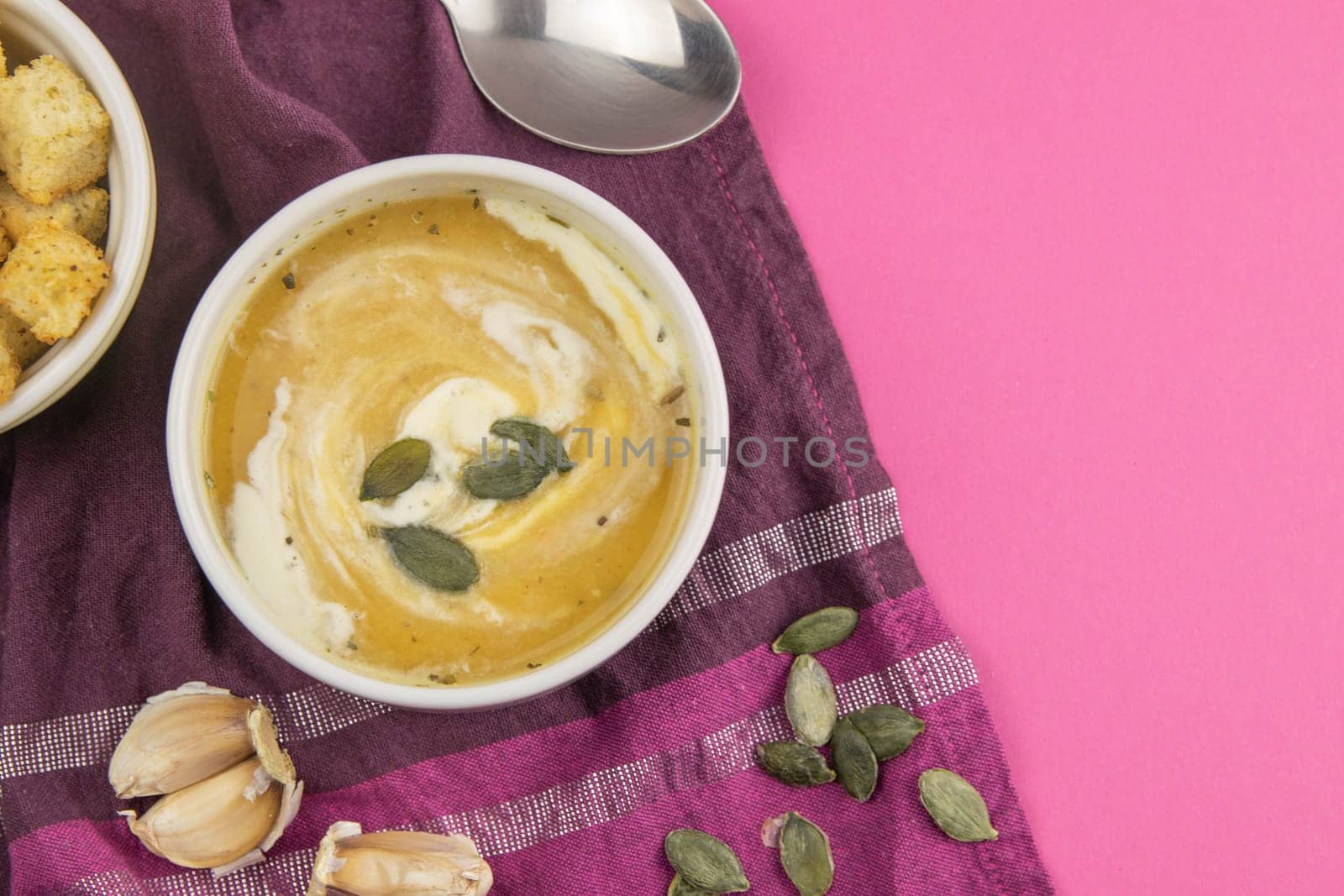 Pea soup with croutons stands on a green towel, next to there are tomatoes, toasts of pumpkin seeds, everything stands on the yellow table.