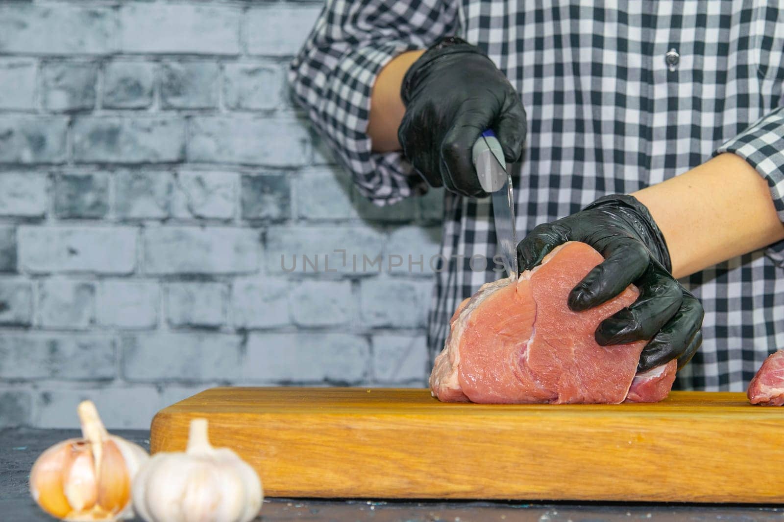 Female hands in black gloves cut juicy slices of pork, garlic stands nearby.