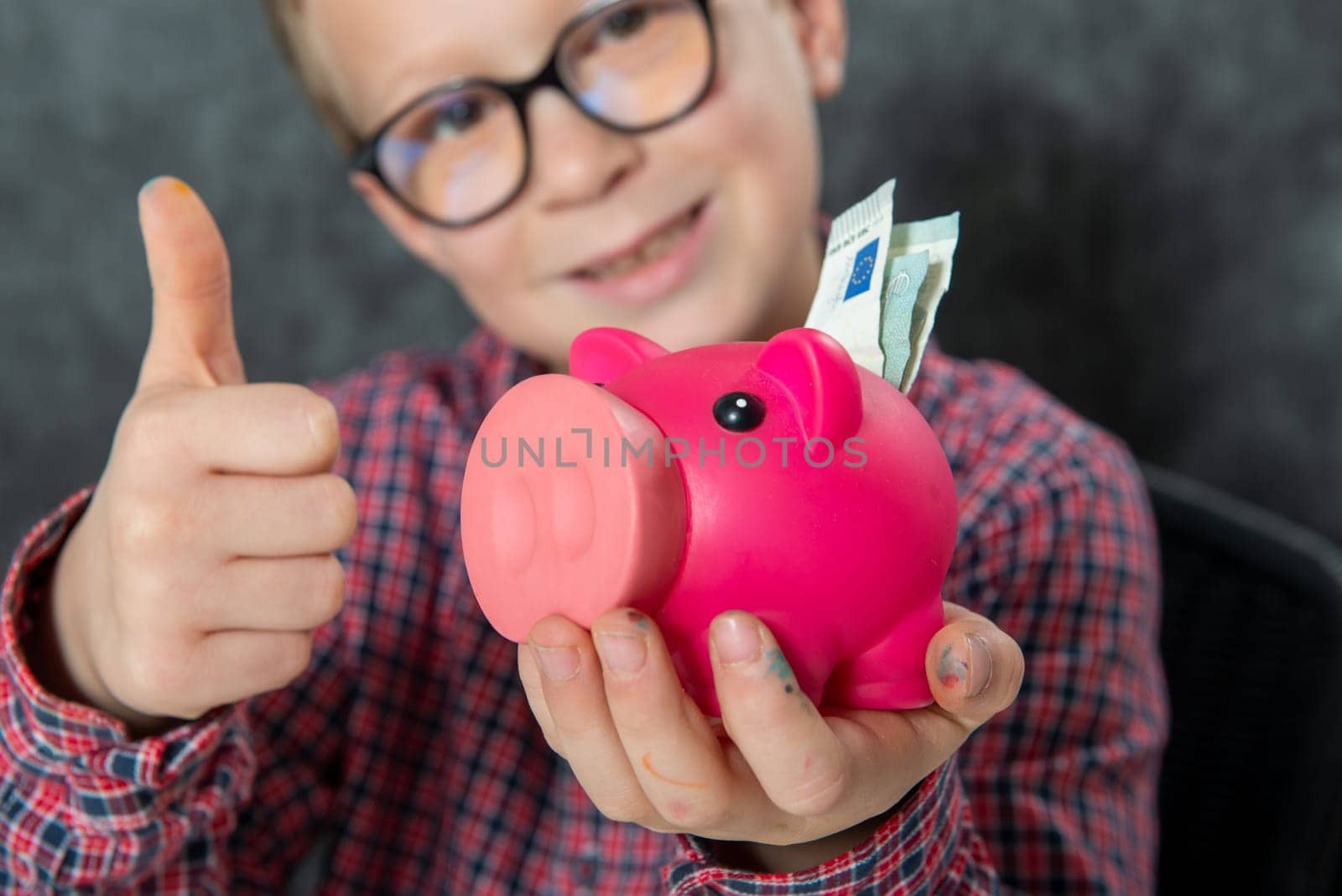 Smile young boy with glasses puts money into a piggy bank