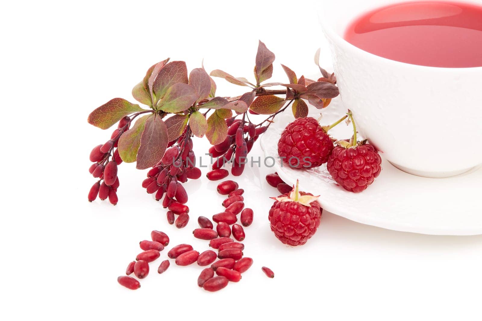 Healthy fruit tea with barberries and raspberries in white cup and branch of berberry isolated on white background.