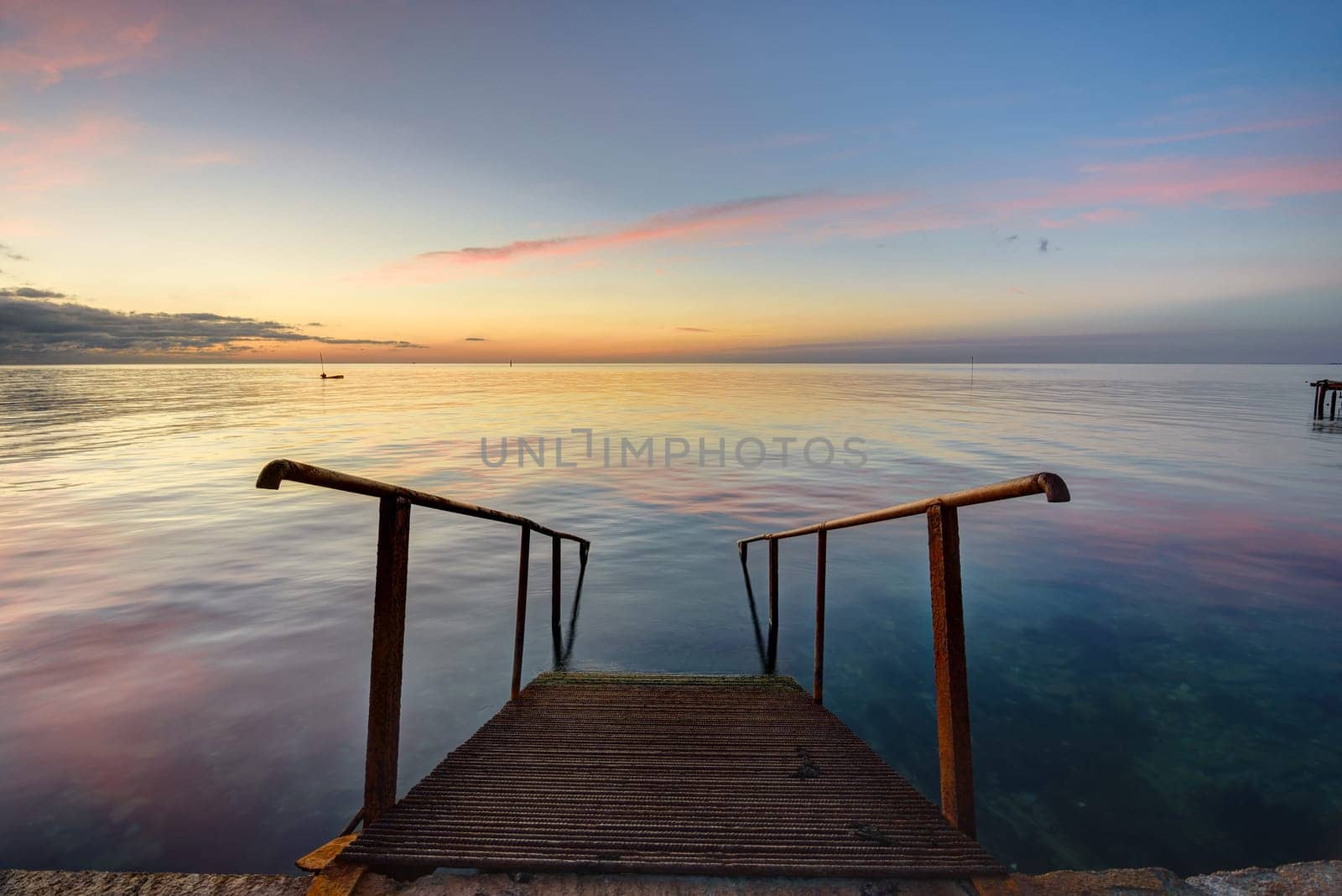 The old mittal staircase on the pier descends into the sea, against the background of the evening beautiful sunset