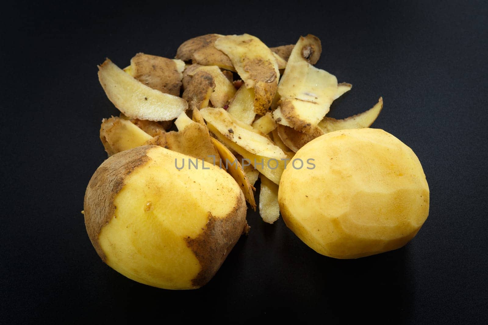 Raw peeled potatoes and potato peelings on black background