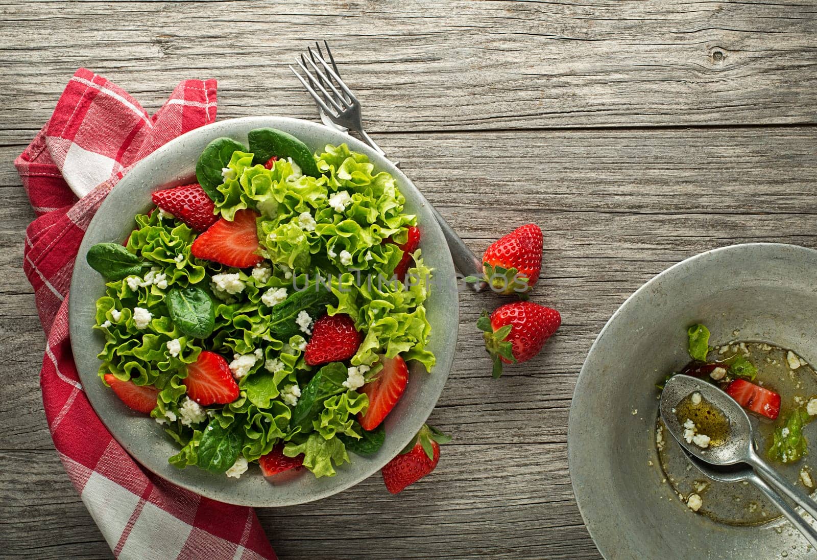 Healthy green salad with strawberry and fresh cheese on wooden table background. Healthy salad meal.