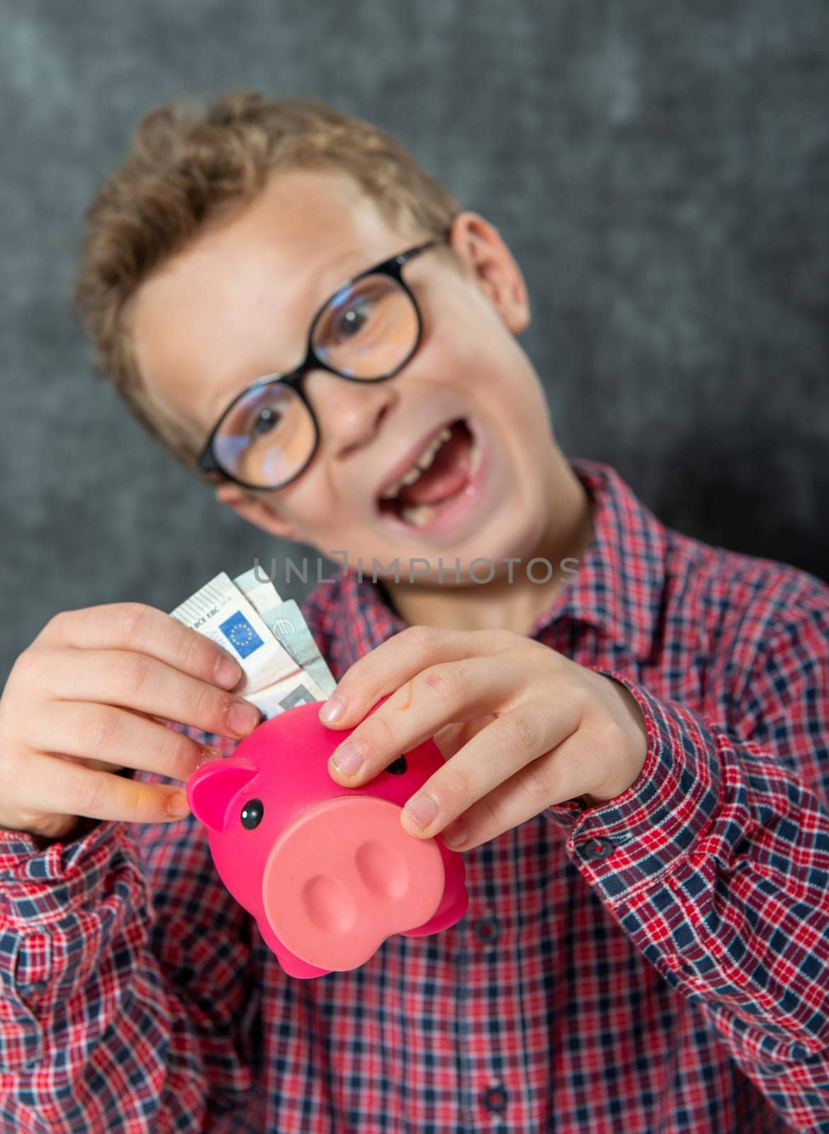 funny young boy with glasses puts money into a piggy bank