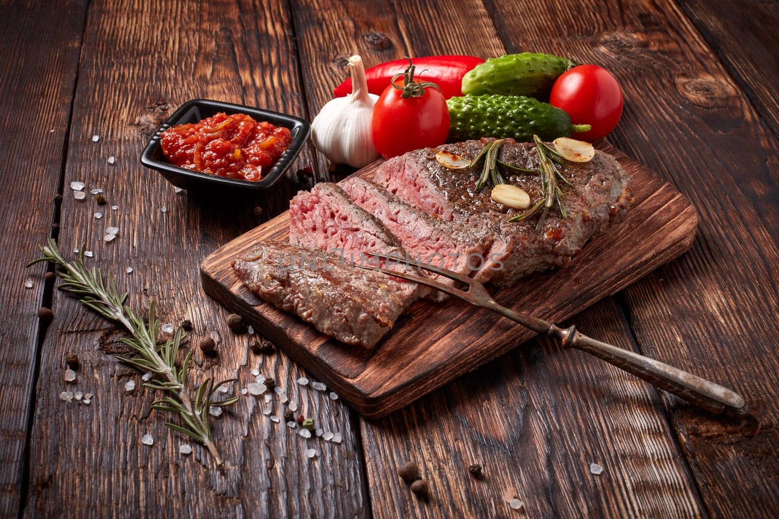 Grilled meat. Medium rare beef steak on wooden cutting board, rosemary twigs, spices and vegatables on brown wooden background. Steak menu