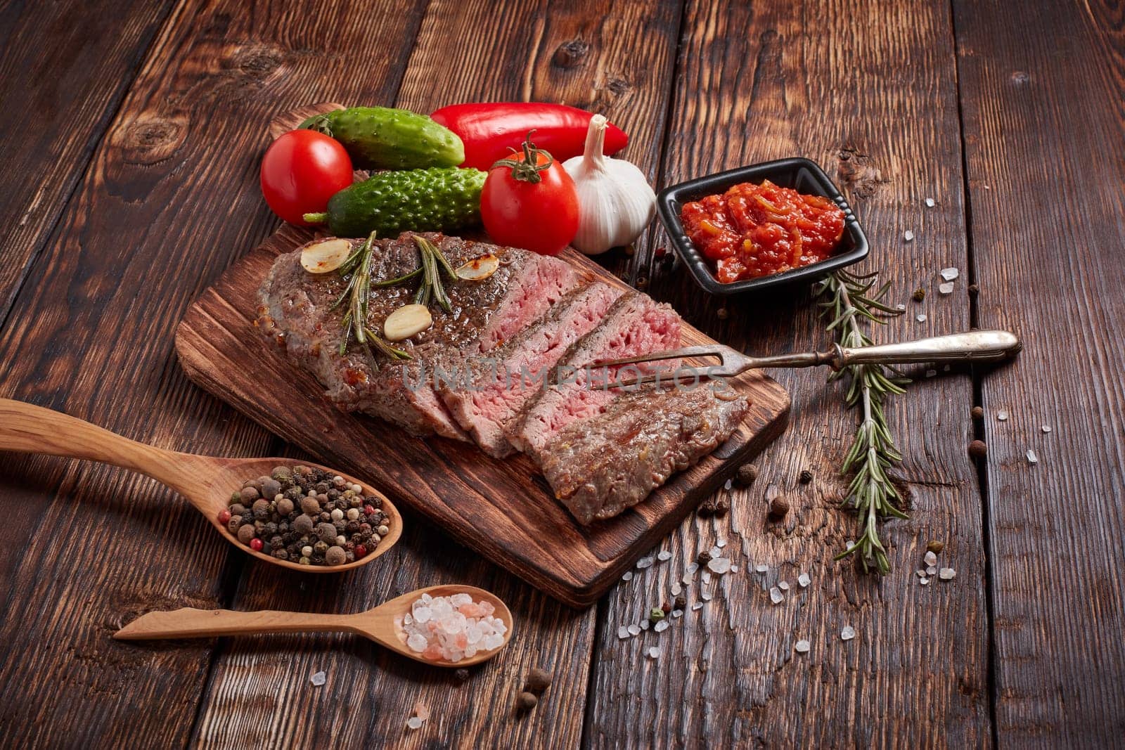 Grilled meat. Medium rare beef steak on wooden cutting board, rosemary twigs, spices and vegatables on brown wooden background. Steak menu