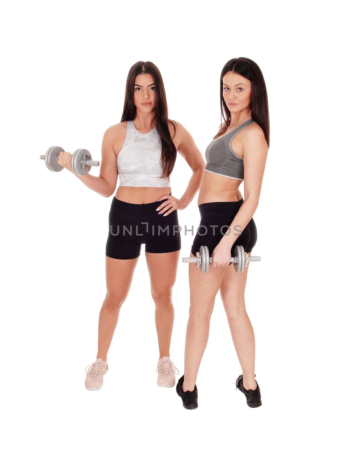 Two young beautiful woman standing in workout outfits in the studio.working out with there dumbbells, isolated for white background.