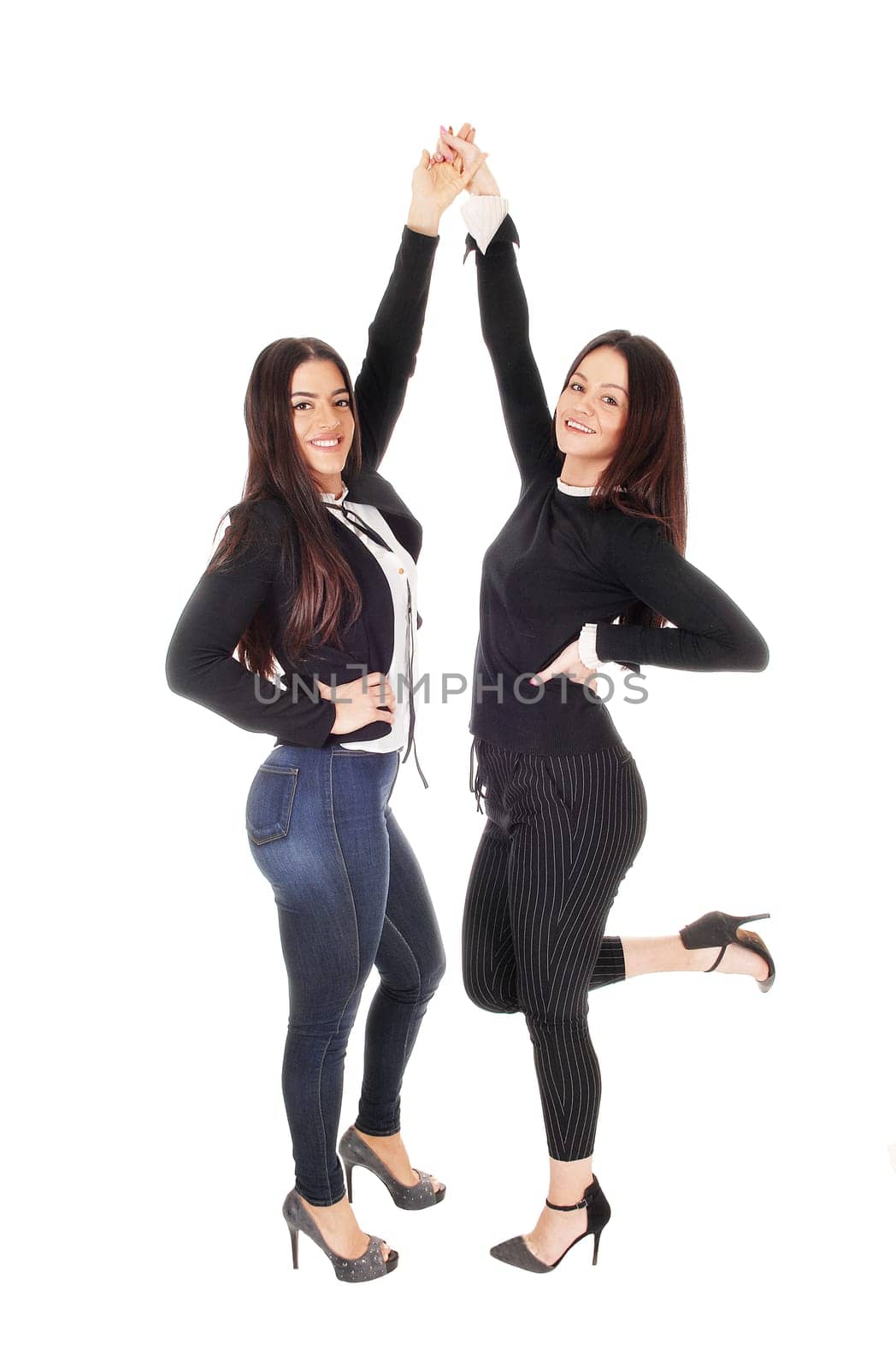 Two beautiful young woman standing face to face in jeans and heels.looking at the camera, lifting there hands, isolated for white background.