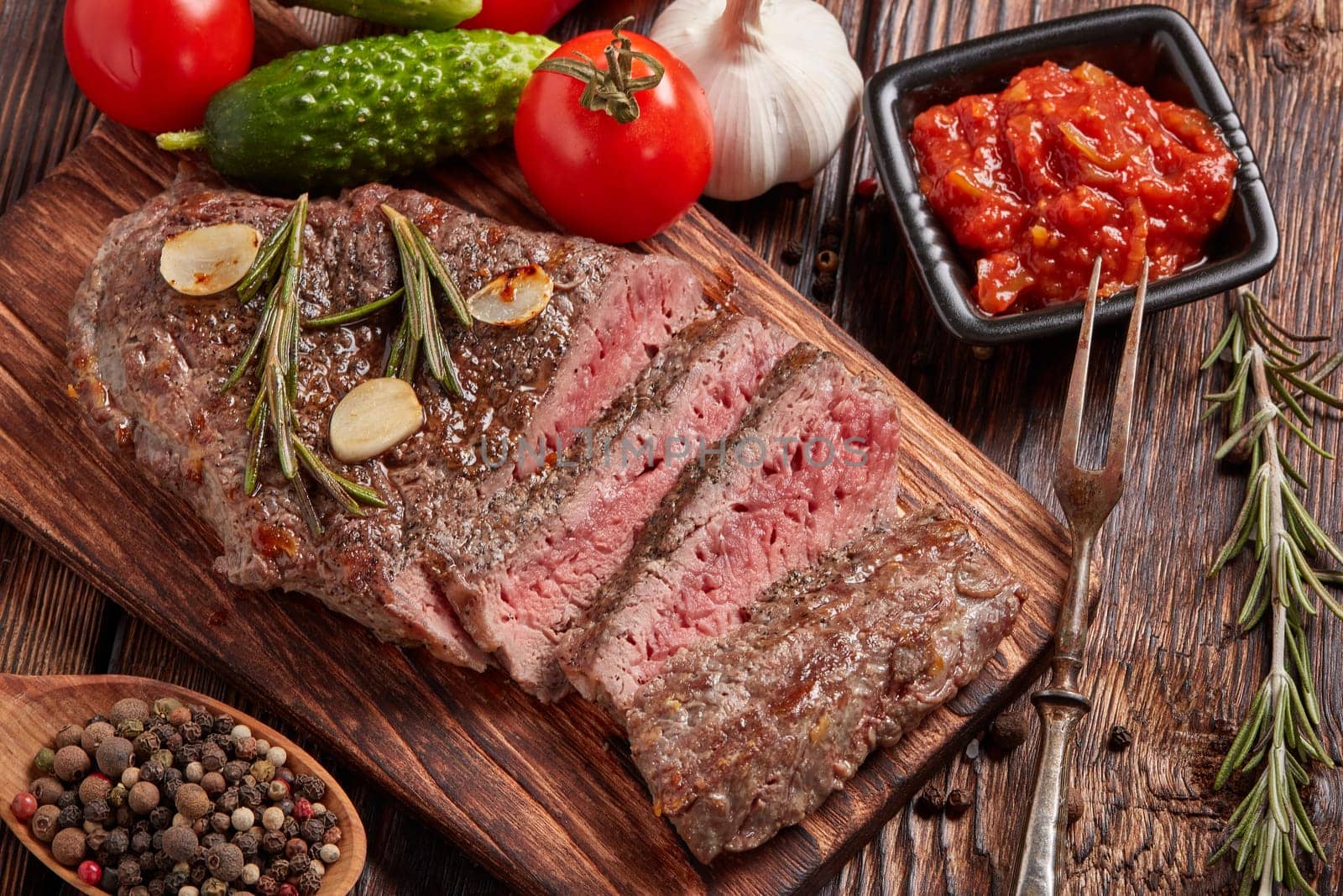 Grilled meat. Medium rare beef steak on wooden cutting board, rosemary twigs, spices and vegatables on brown wooden background. Top view. Steak menu