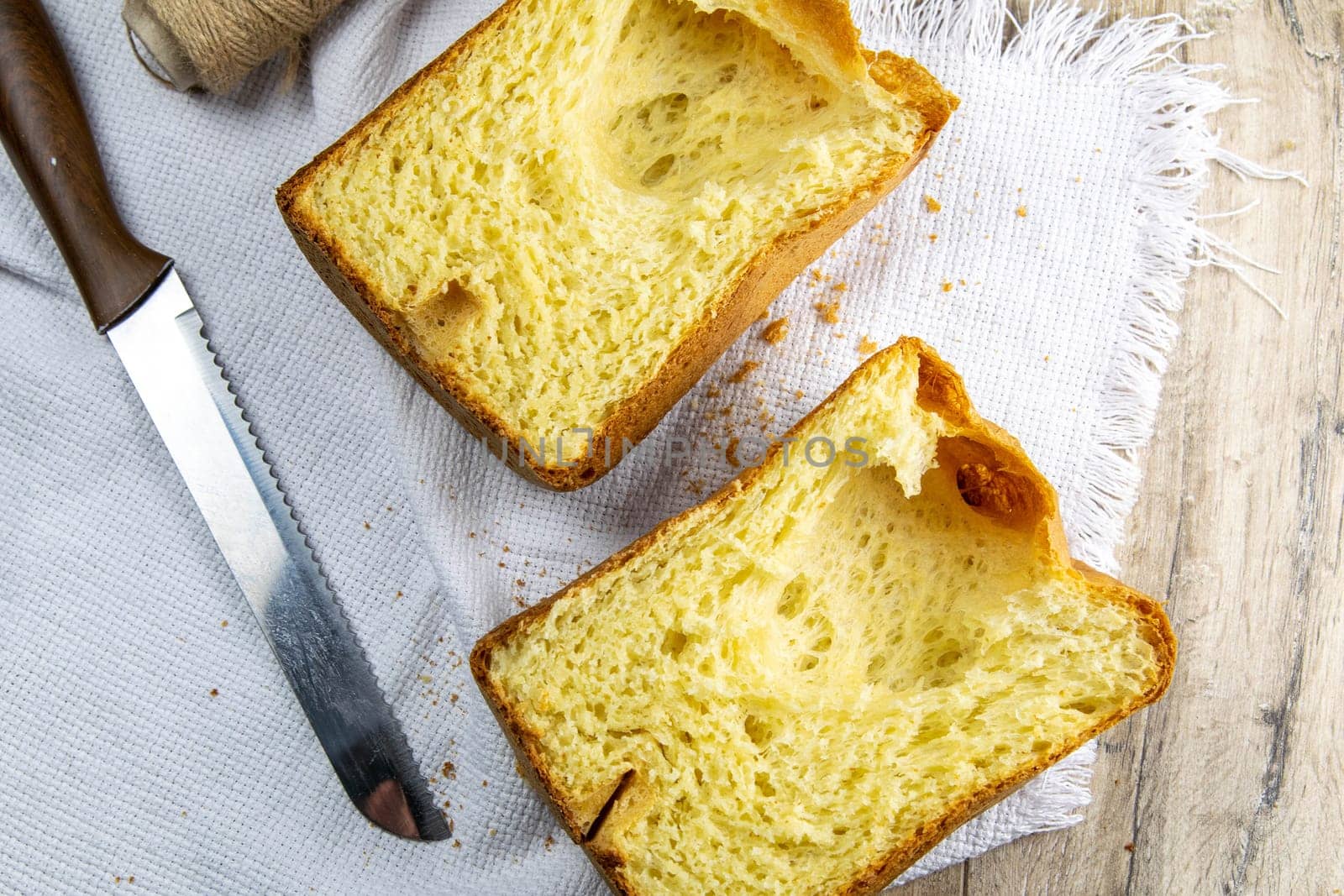 Fresh homemade bread stands on a white towel on a wooden board, next to a knife for cutting bread. Top views.