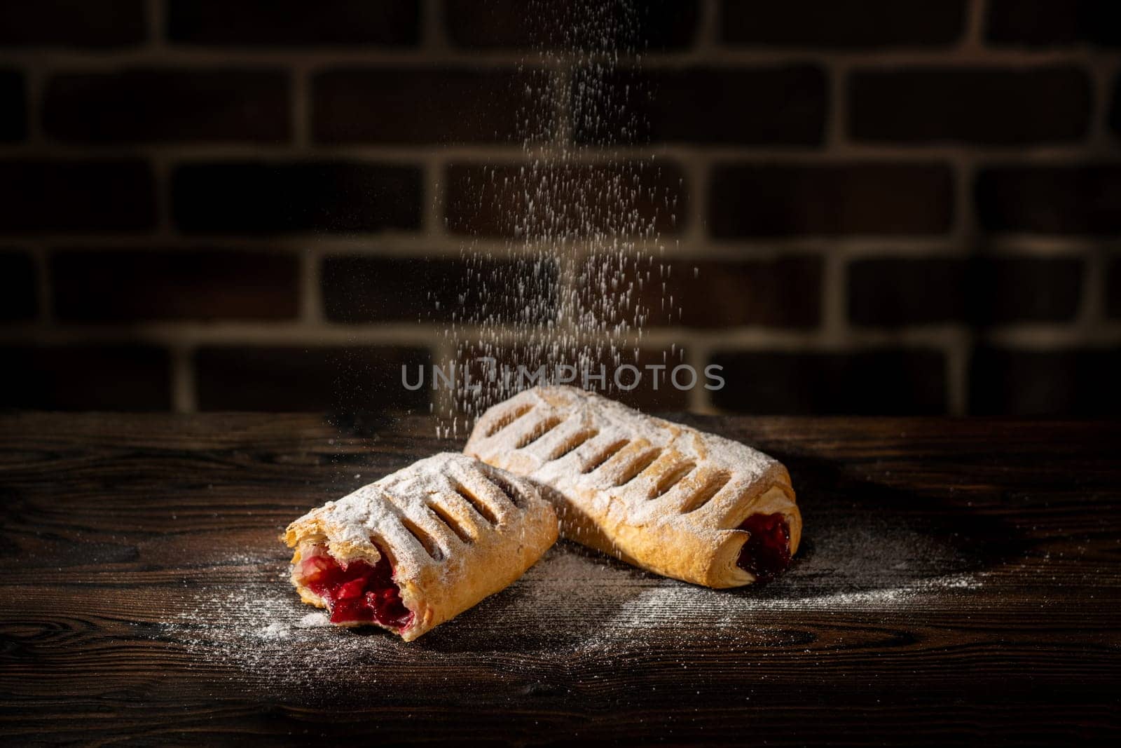 Strudel with cherries powdered with sugar on a wooden table and brick background
