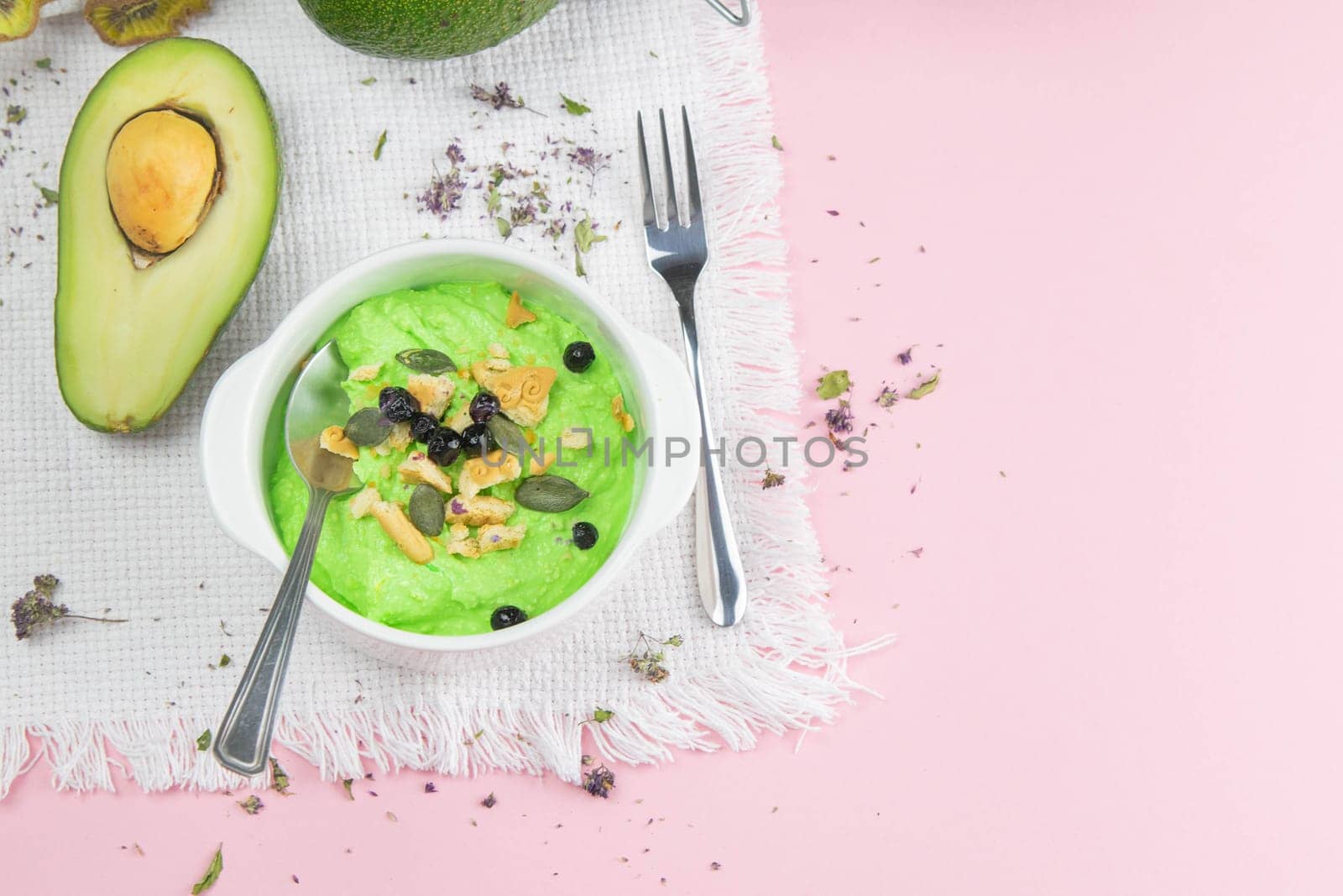 Two curd desserts: one with blueberries and nuts and the other with avocado and kiwi, next to there are pumpkin seeds and nuts.