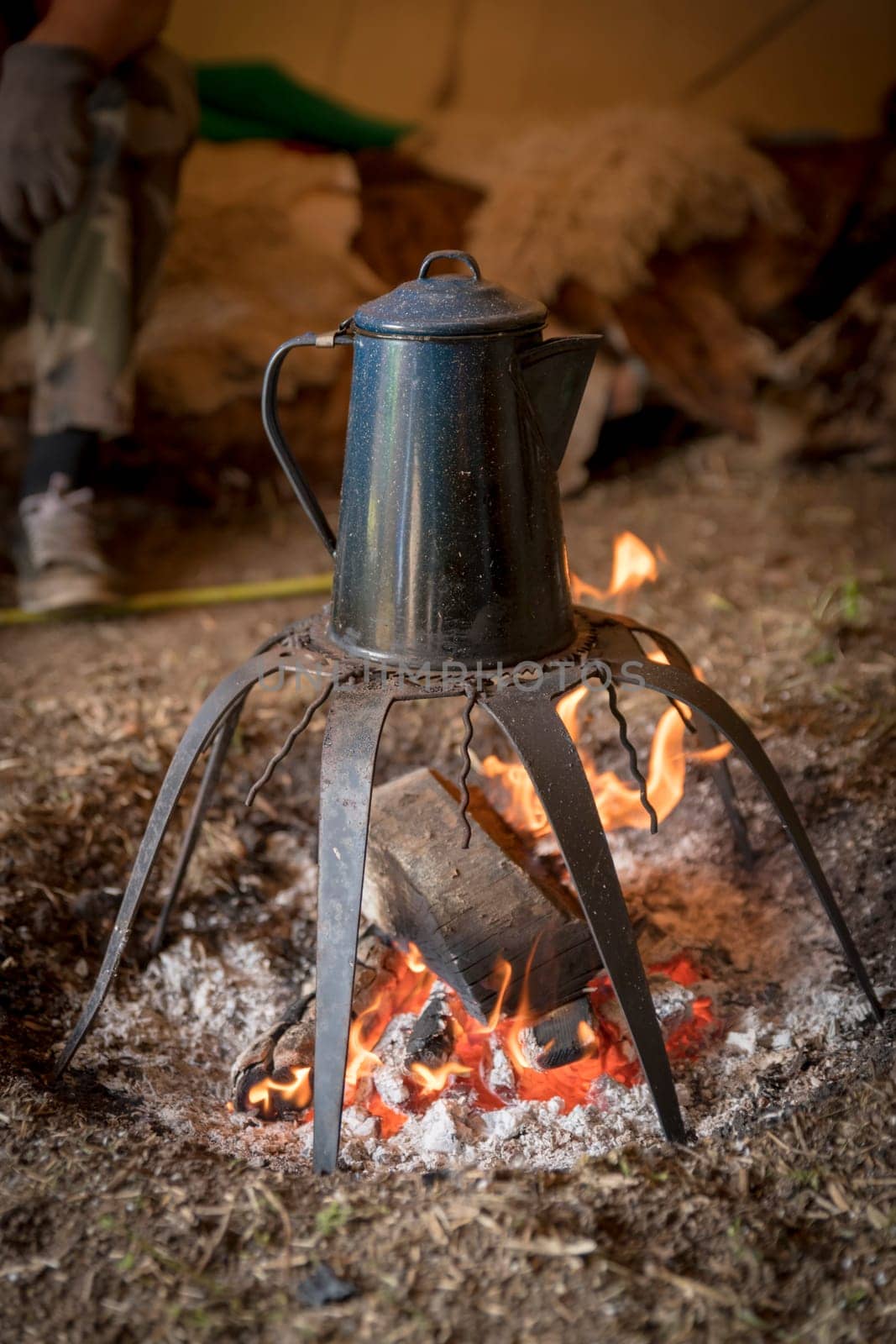 Old metal coffee pot stands over a campfire on a rack