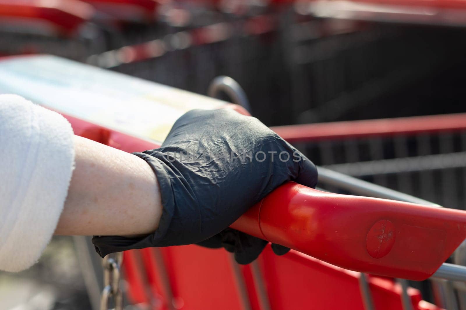 Hand, black glove on the handle of a Shopping cart