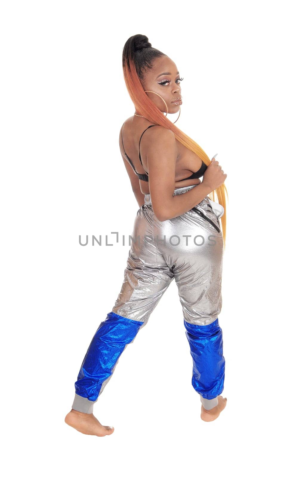 A gorgeous African American woman standing in silver pants and a black.bra, from the back, looking over shoulder, isolated for white background.