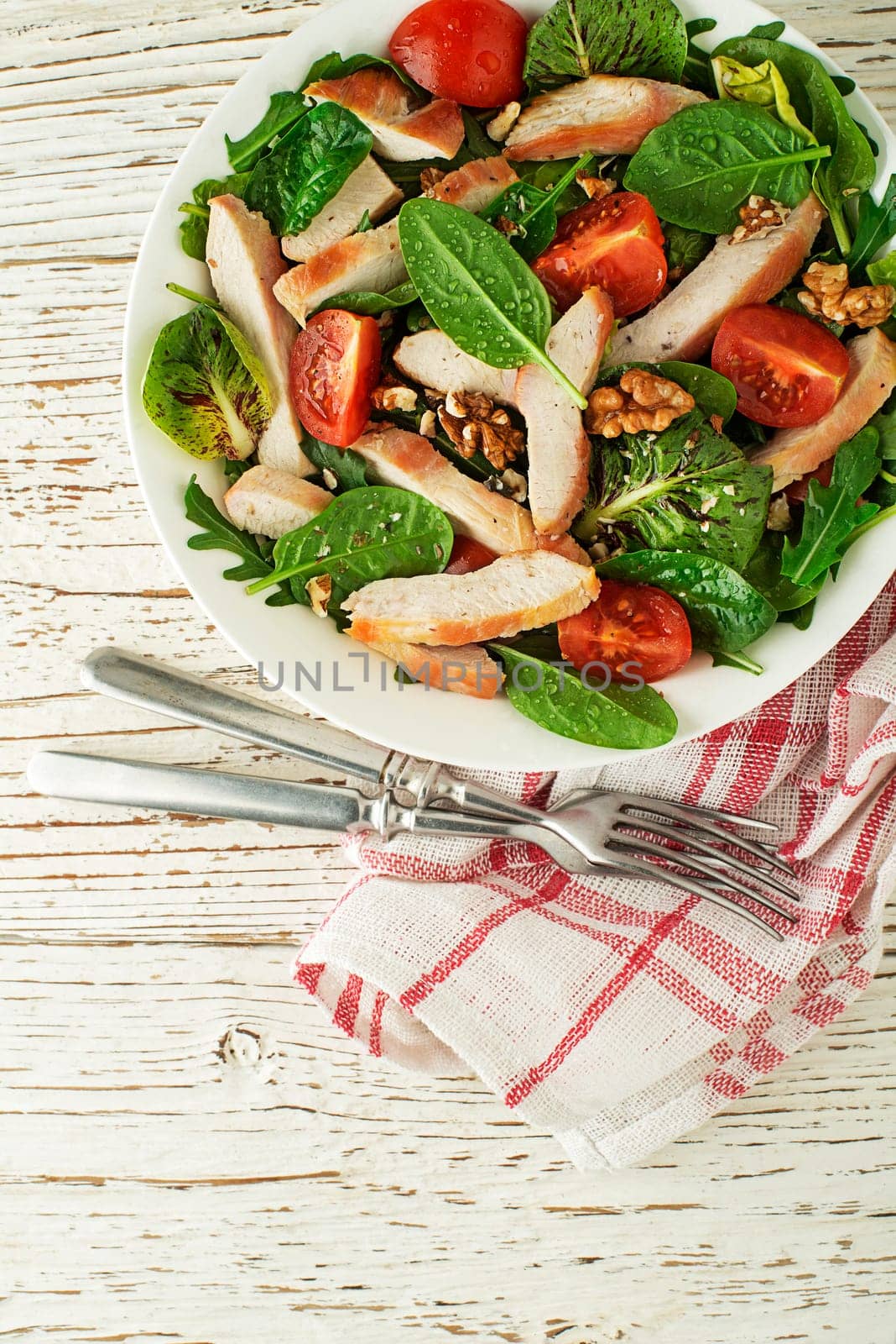 Healthy green salad with chicken breast tomato and nuts on wooden table