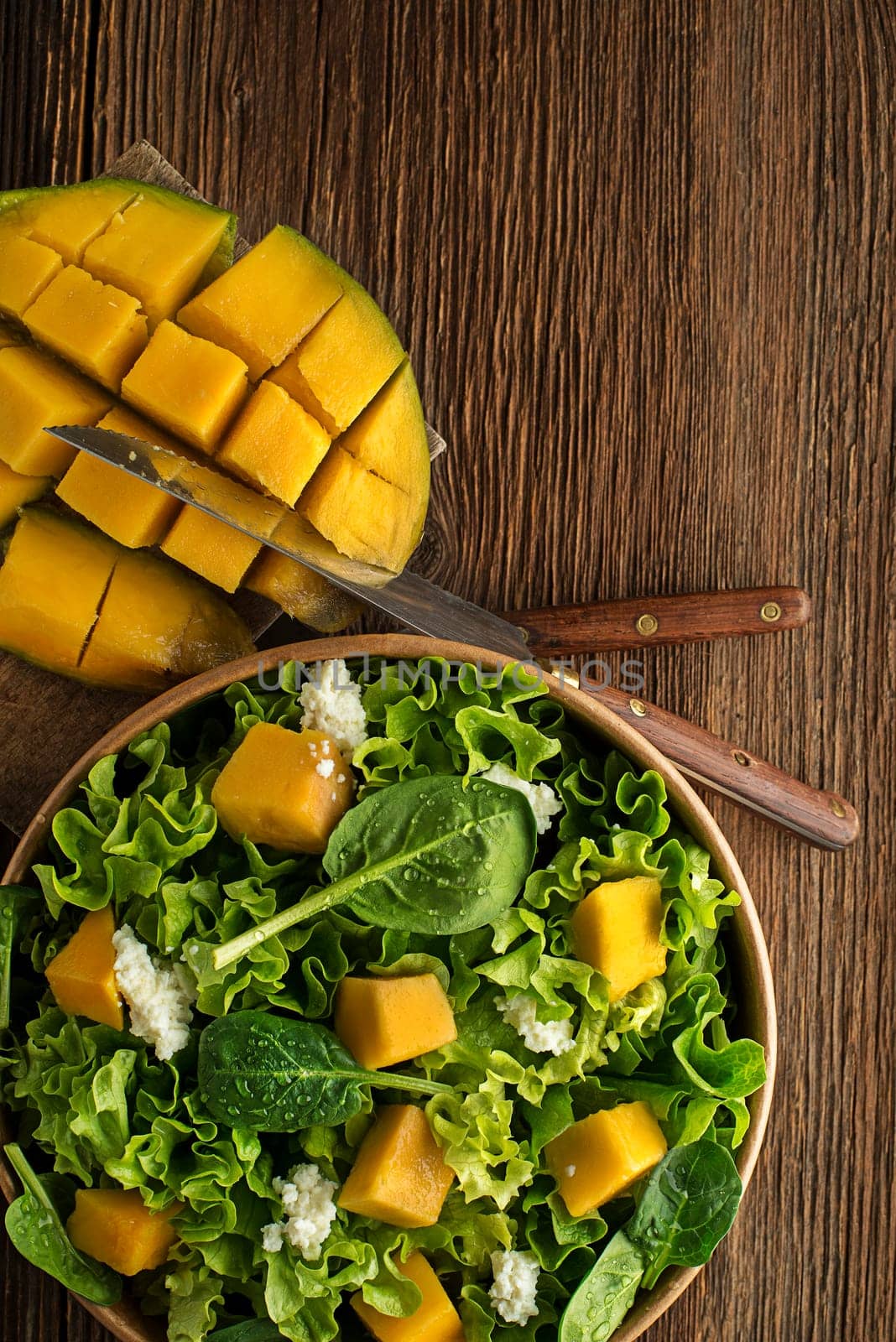 Healthy green salad with mango fruit and fresh cheese on wooden table background. Healthy salad meal.