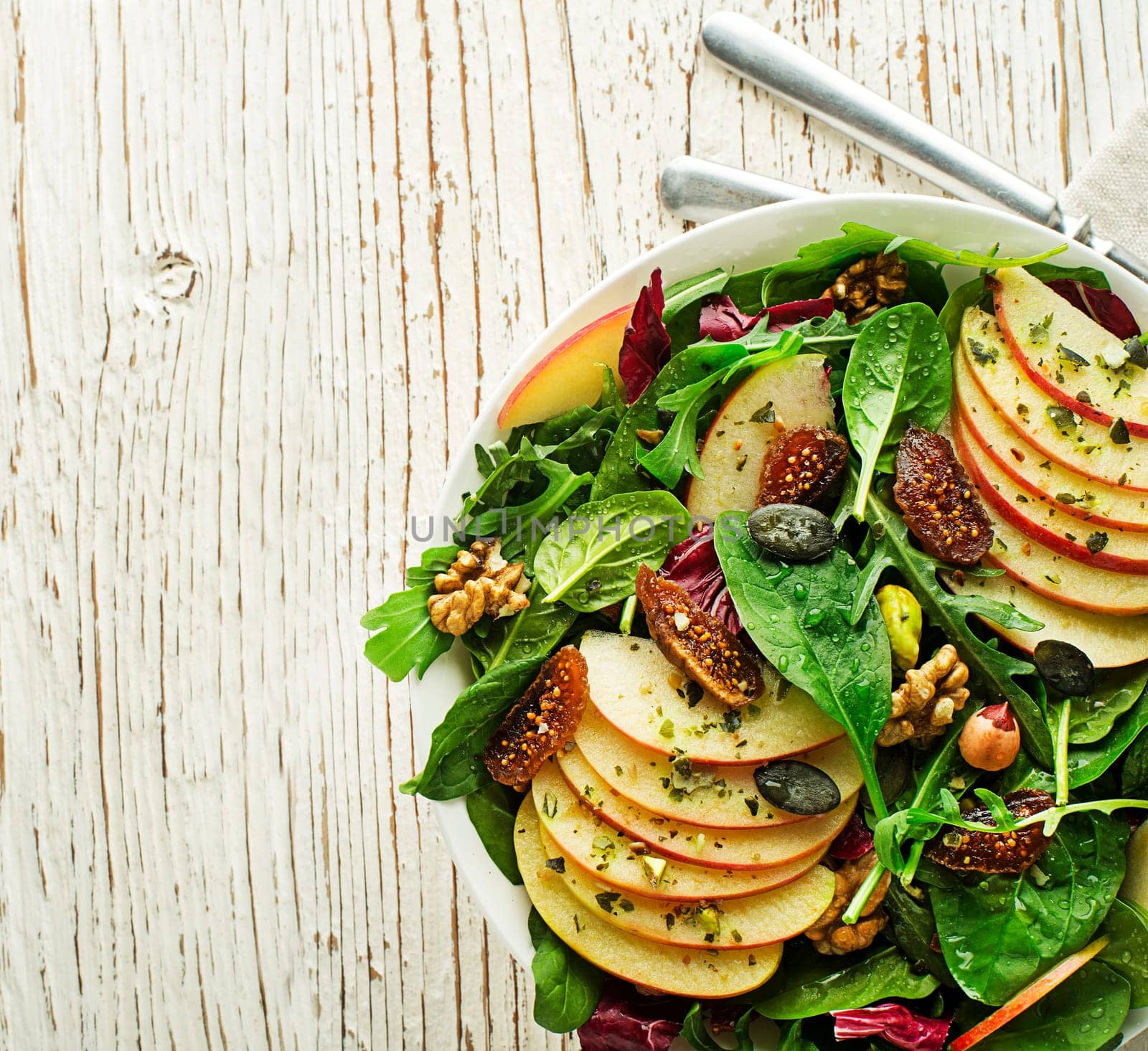 Healthy green salad with apple fruit, seeds and nuts on wooden table