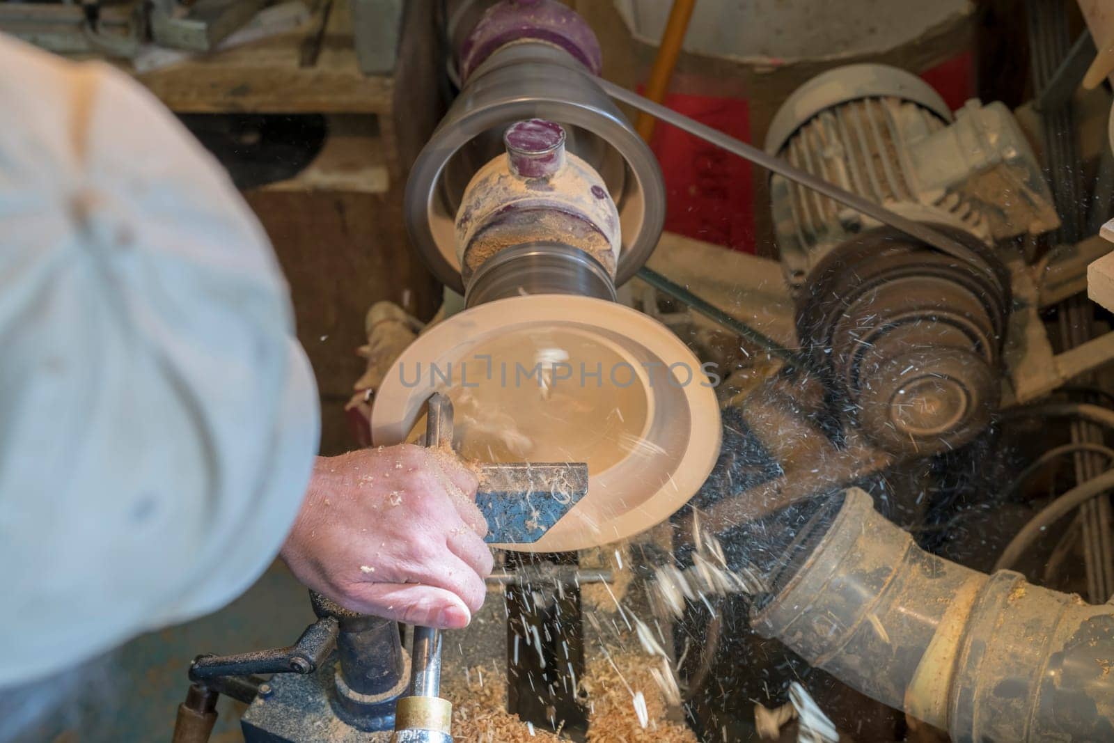 Making a wooden bowl on a lathe in an old small workshop with flying wooden shavings