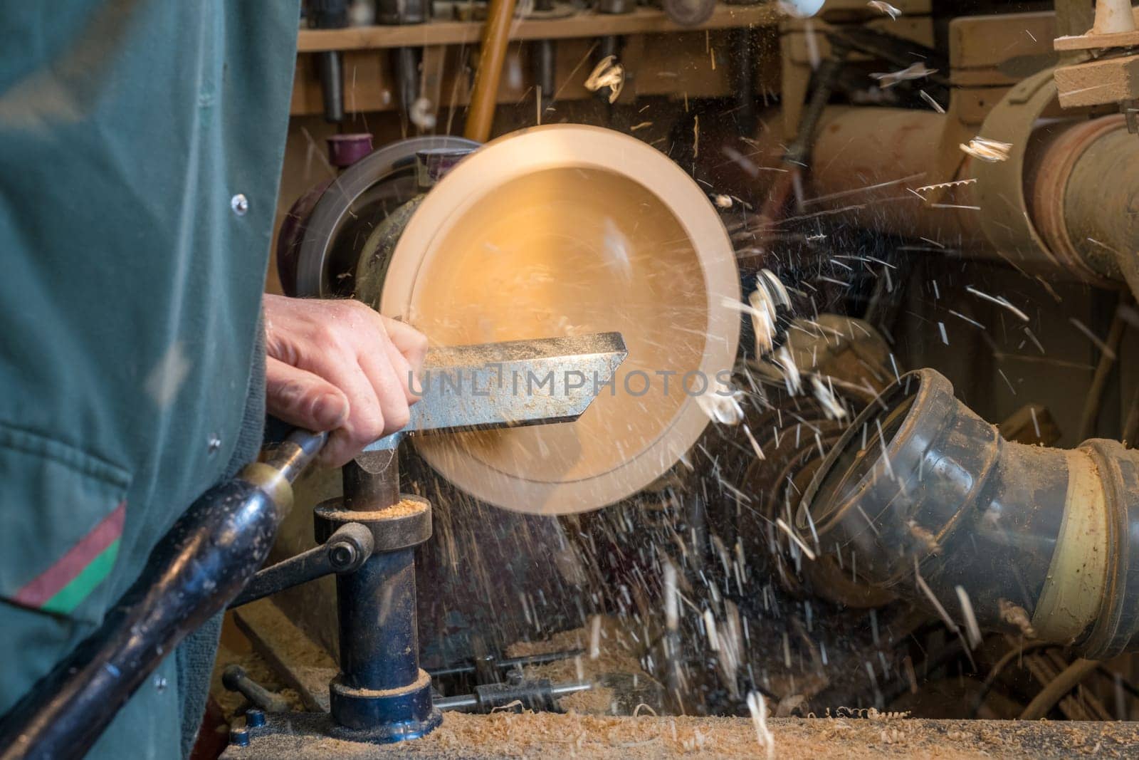 Making a wooden bowl on a lathe in an old small workshop with flying wooden shavings