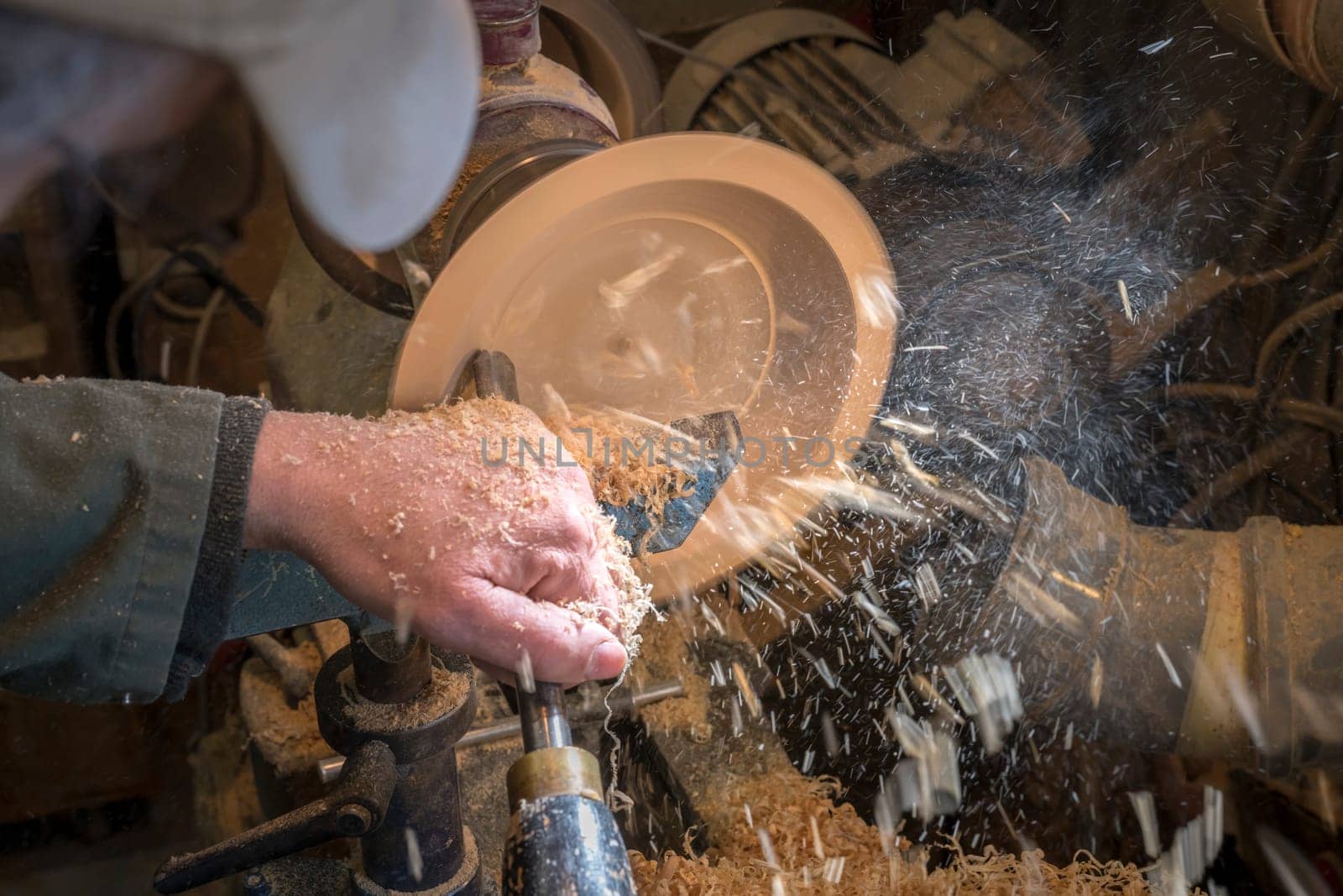 Making a wooden bowl on a lathe in an old small workshop with flying wooden shavings