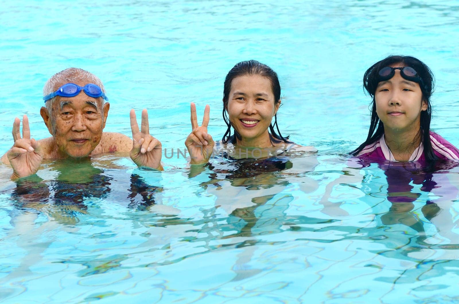 Mother, grandfather and young girl in a swimming pool, looking at camera