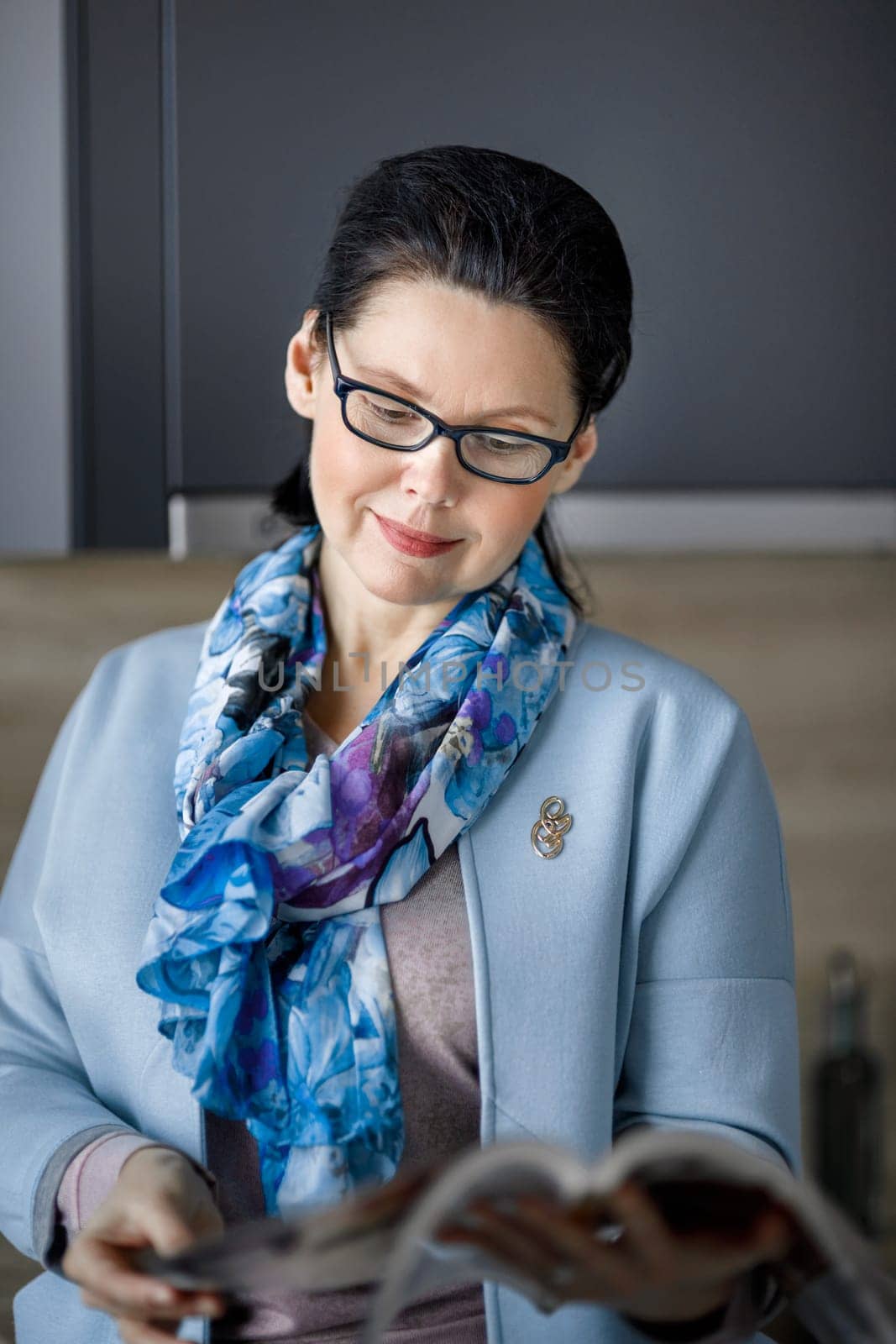 Middle-aged brunette woman reading a magazine with interest.