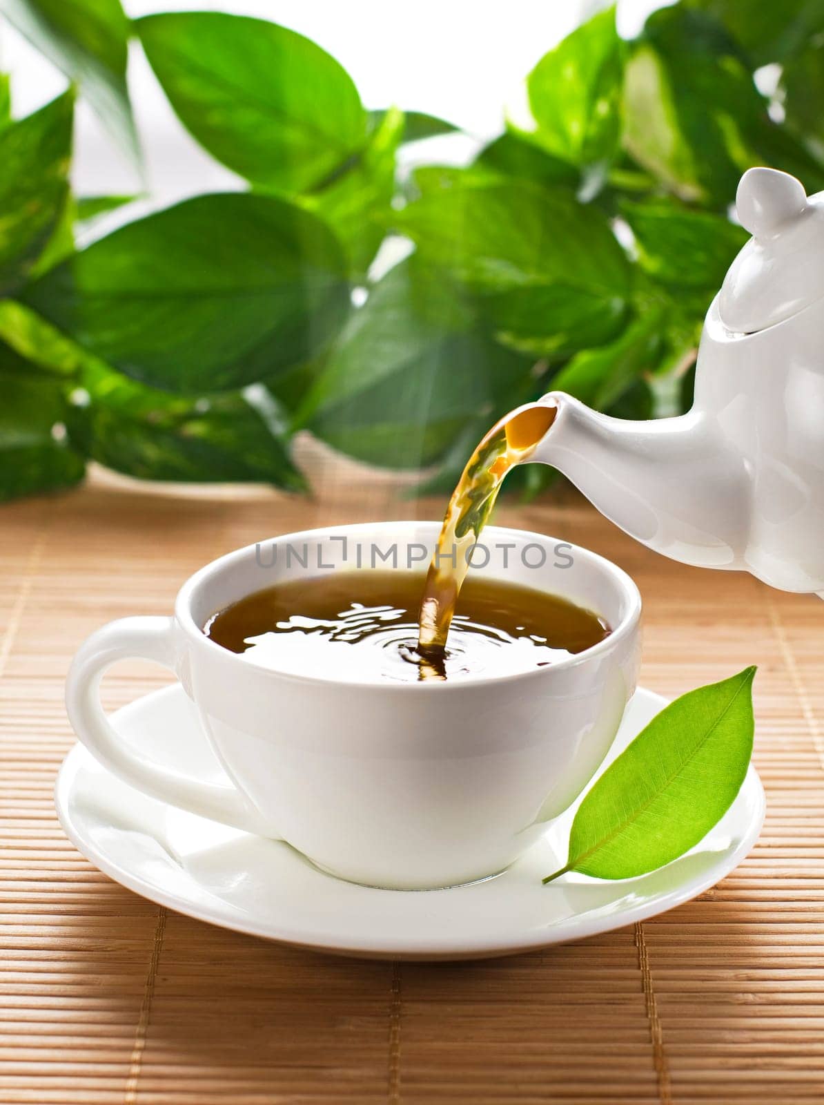 Teapot pouring fresh hot tea in to Cup, on garden background. The Time of Tea Break.
