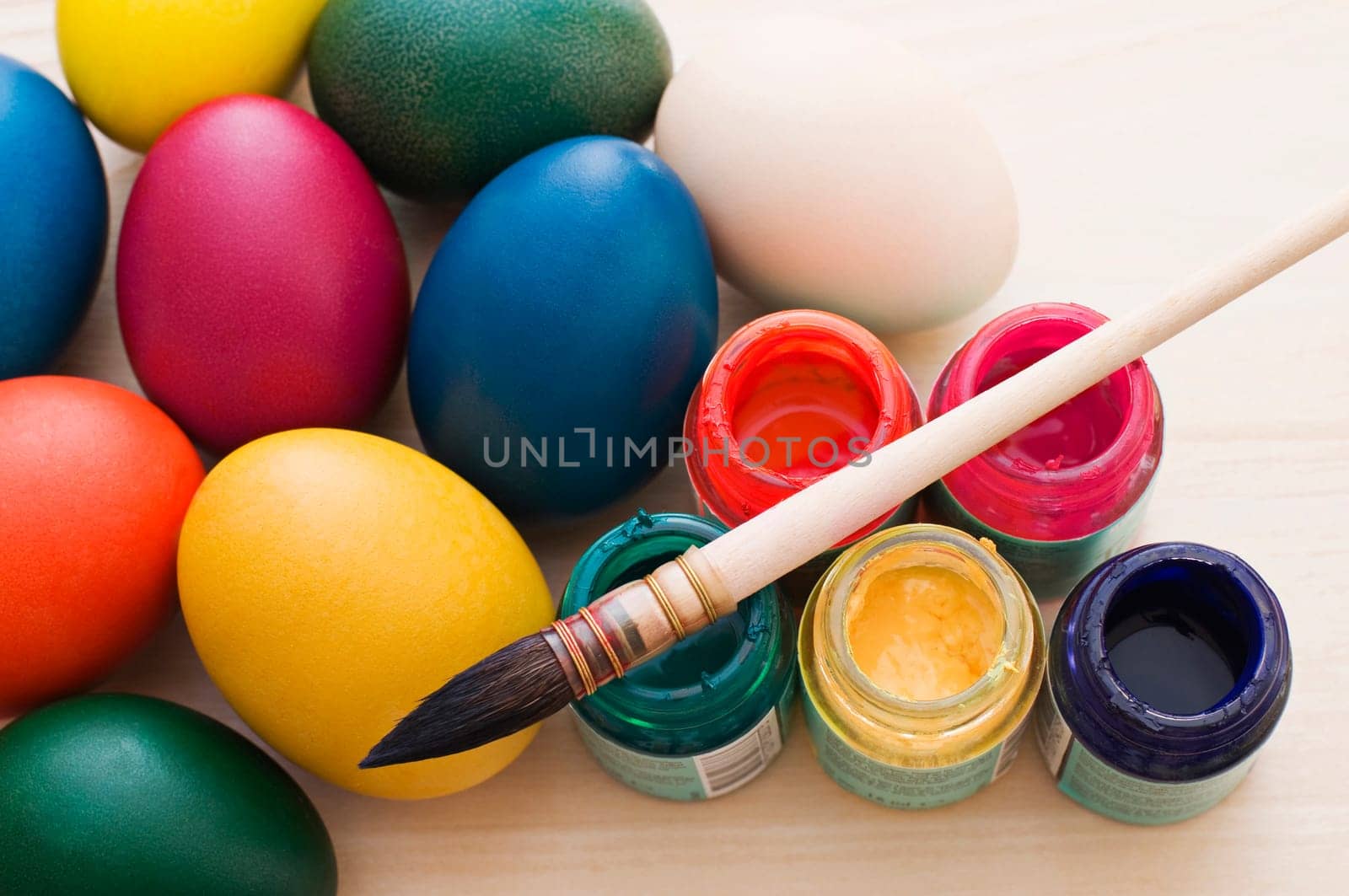 Coloring Easter eggs with a brush and paint on wooden table