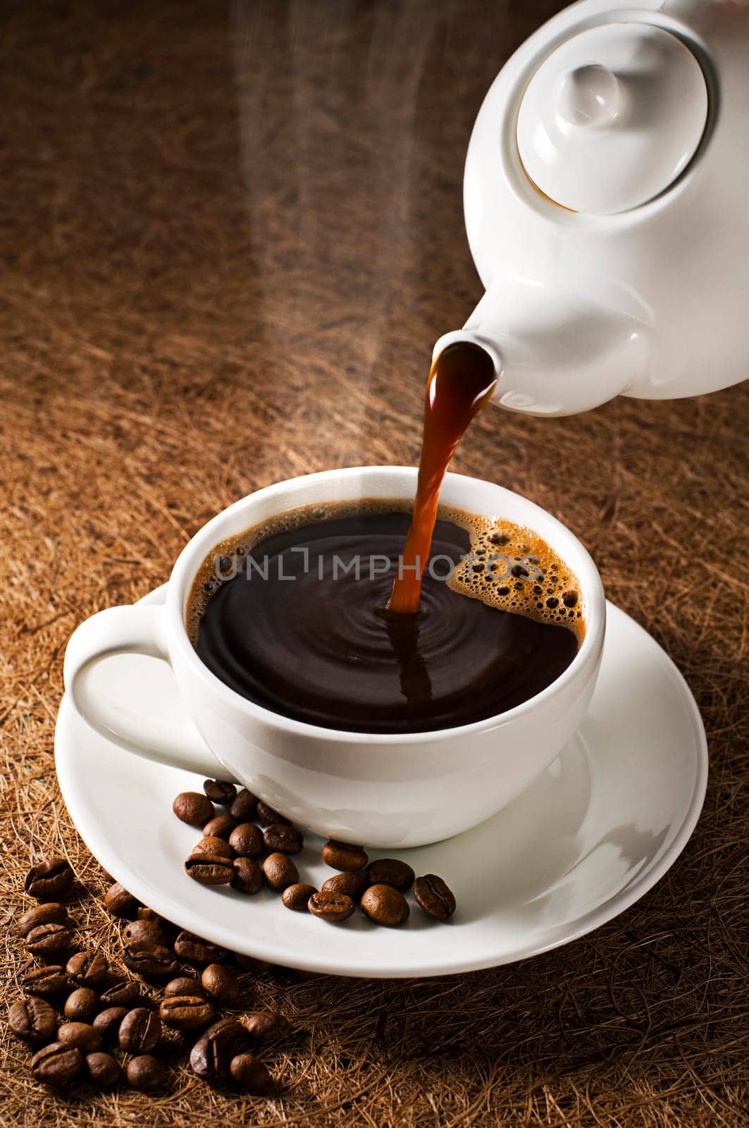 Coffee pot pouring fresh hot coffee into cup on dark background