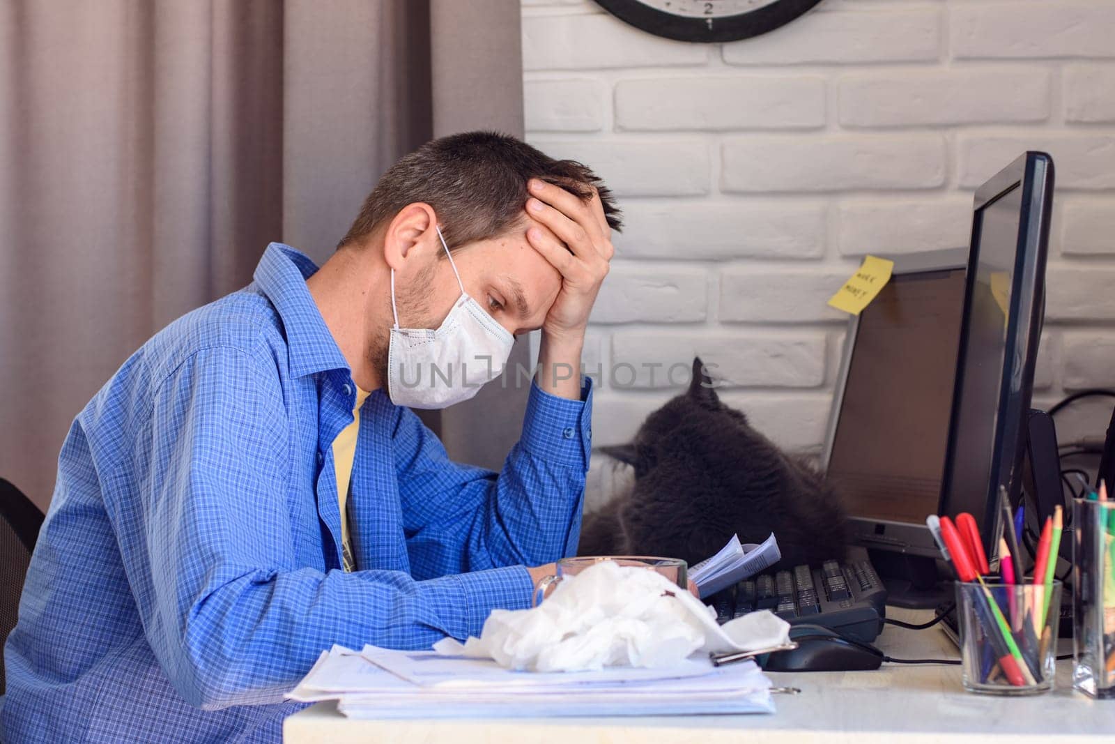 A man in a protective medical mask sits at a computer in a home stop and reads documents