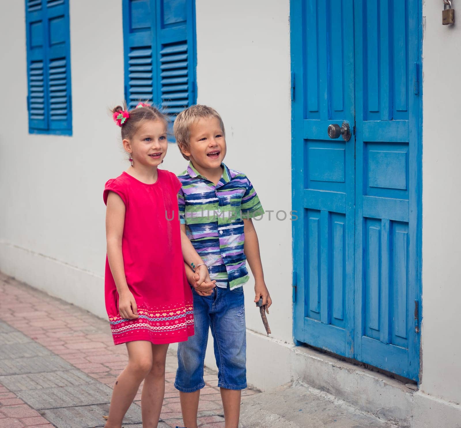 Kids walking by the street next to shutter blue window