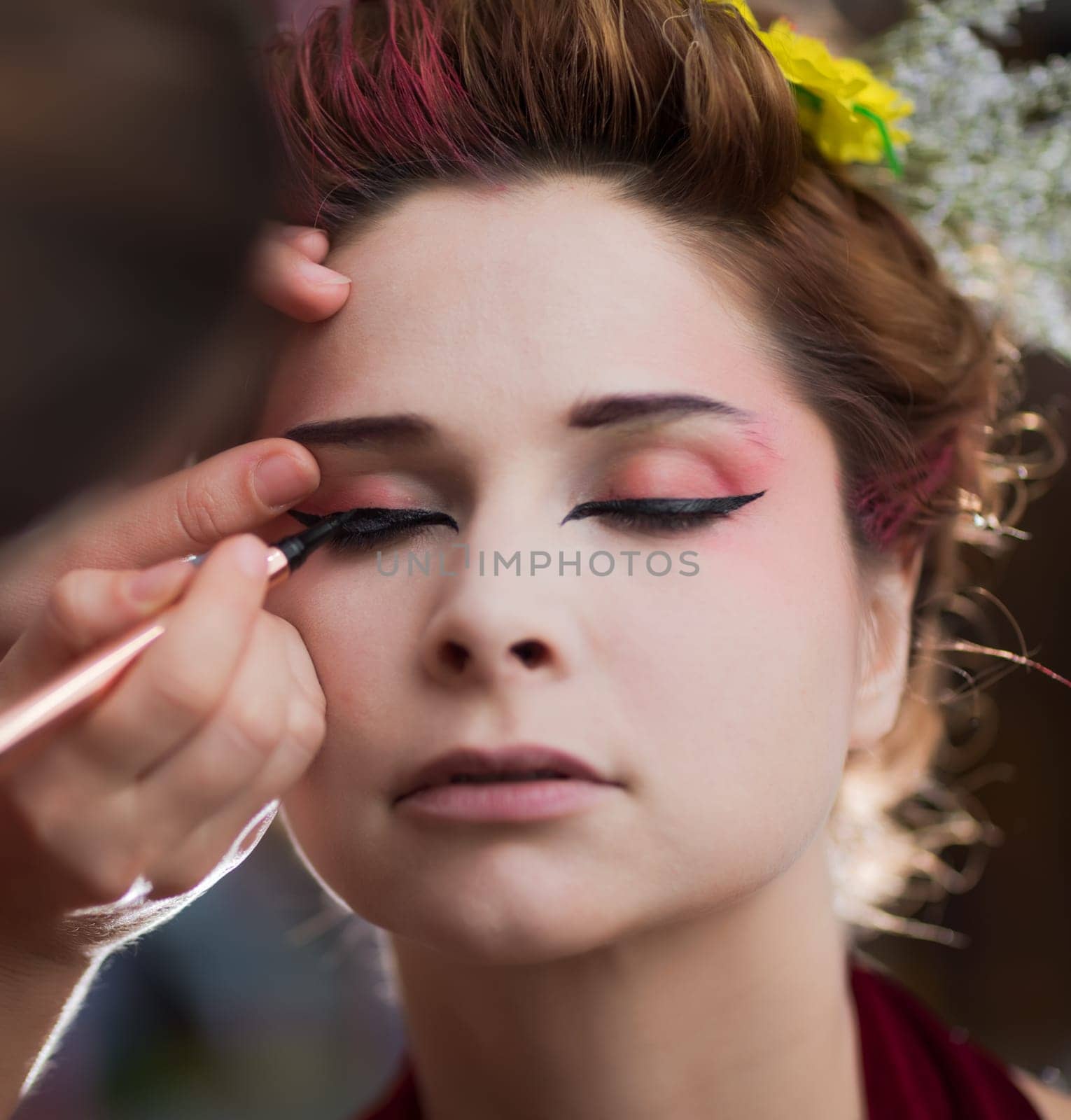 Portrait of a beautiful woman in beauty salon. Makeup artist applies eyeliner on a face