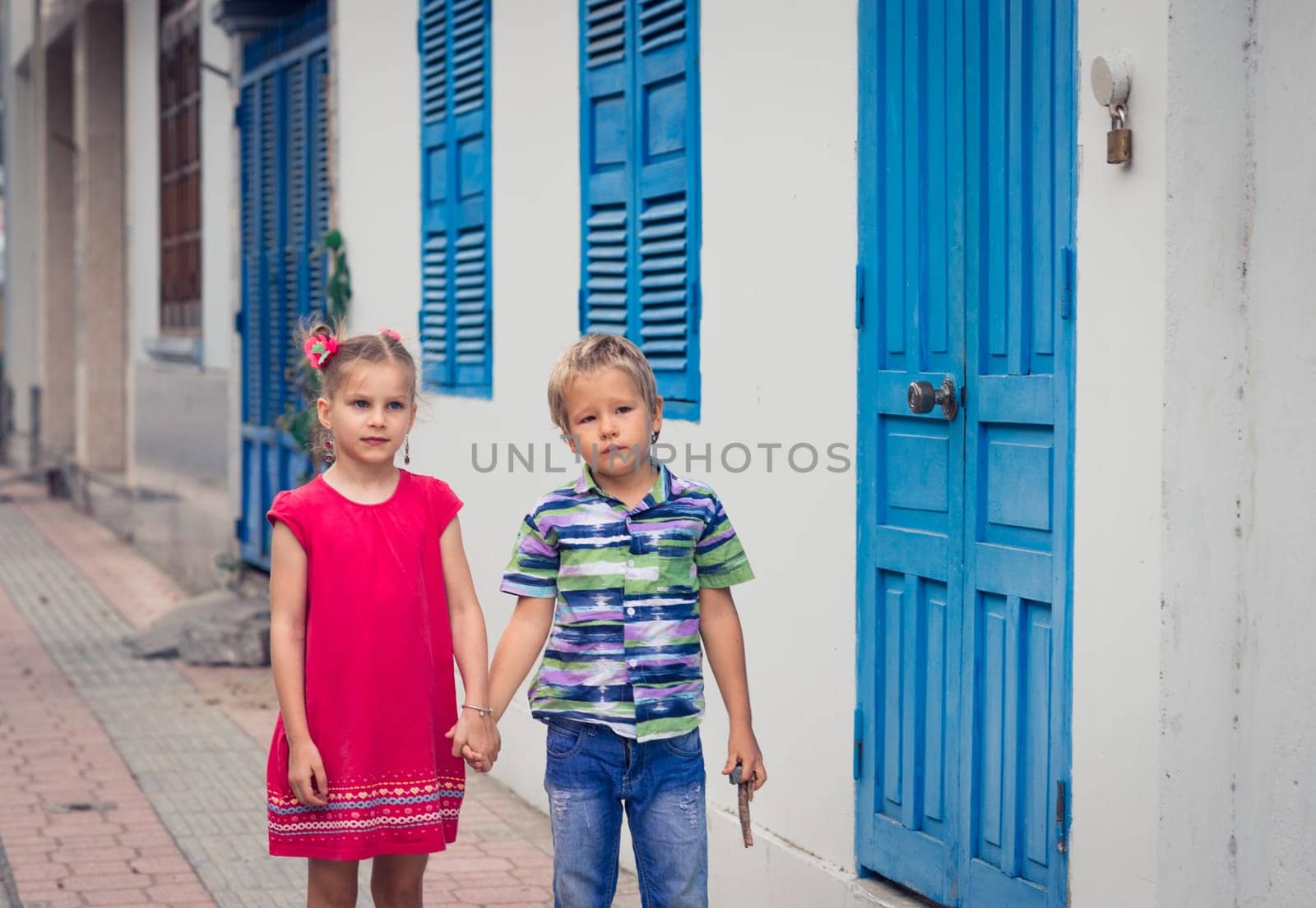 Kids walking by the street next to shutter blue window