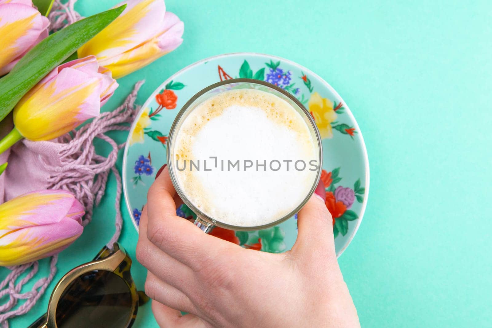 Woman's hand takes cup latte coffee in elegant transparent glass with whipped cream on the mint background.