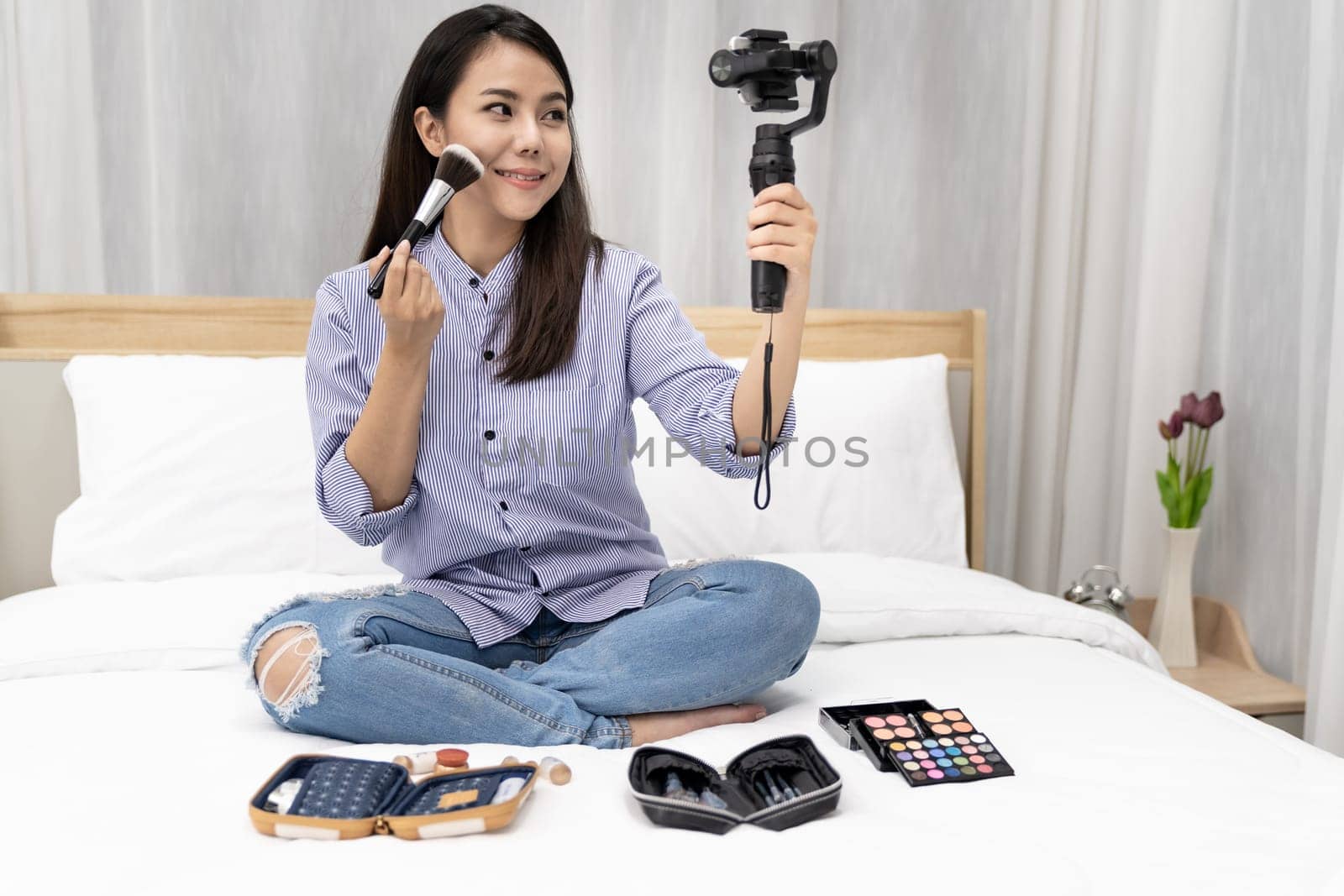 Young beautiful Asian woman beauty vlogger blogger recording live how to make up tutorial to share on social media using Gimbal Stabilizer on mobile phone. Use for vlog social media influencer concept
