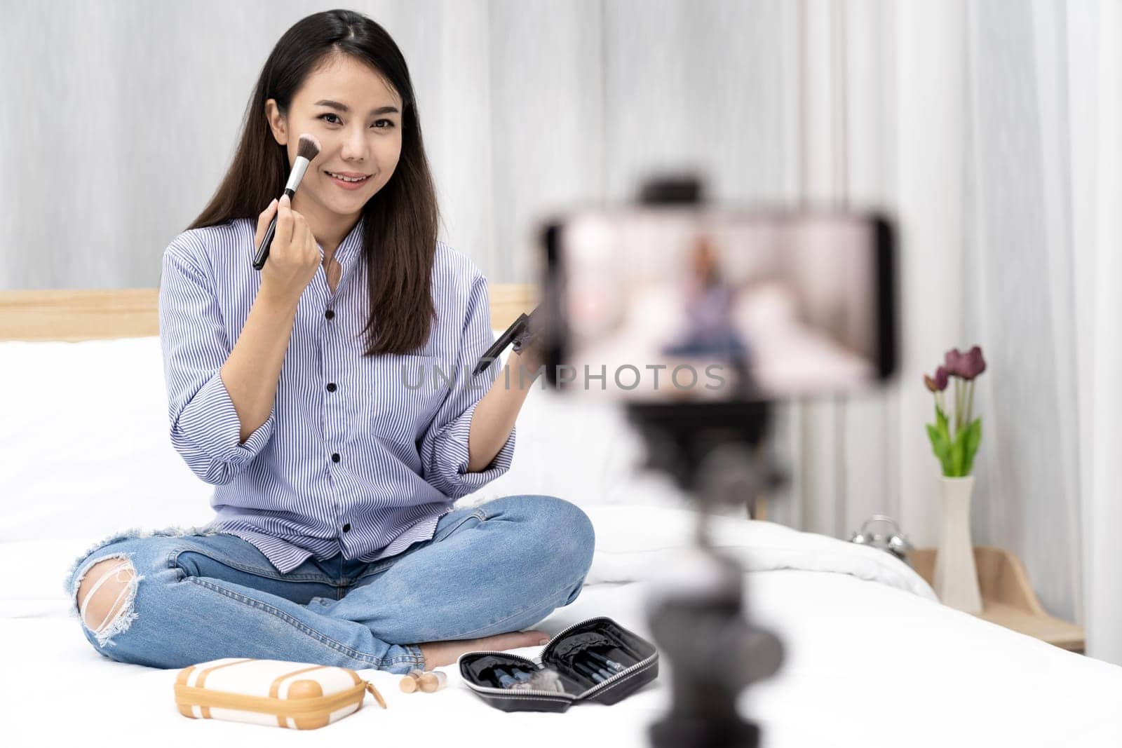 Young beautiful Asian woman beauty vlogger blogger recording live make up tutorial share on social media using digital camera on tripod. Using for vlog social media influencer concept.