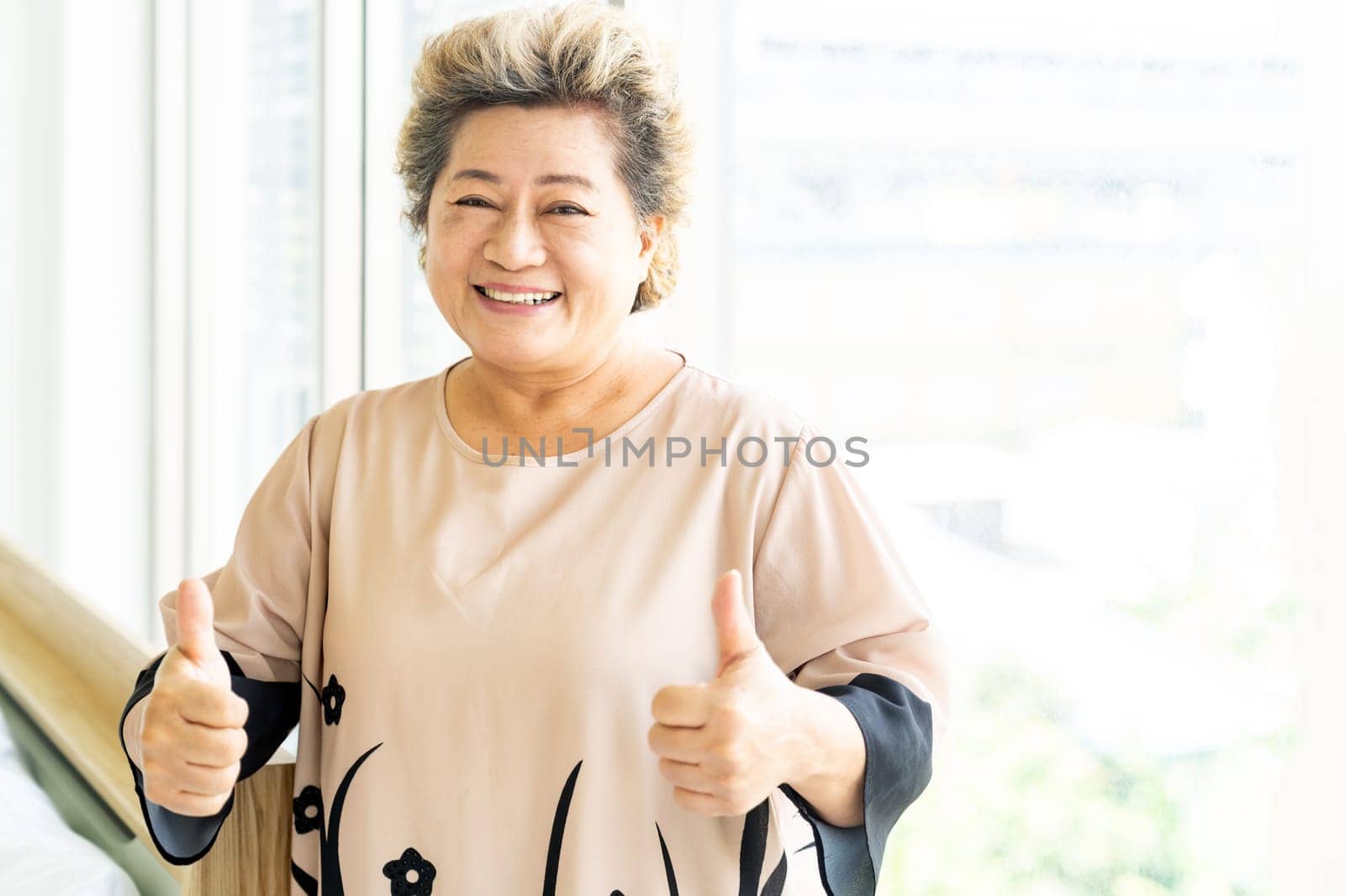 Portrait of happy and smile elderly senior adult female standing beside window in domestic living room - recovery and rehabilitation concept