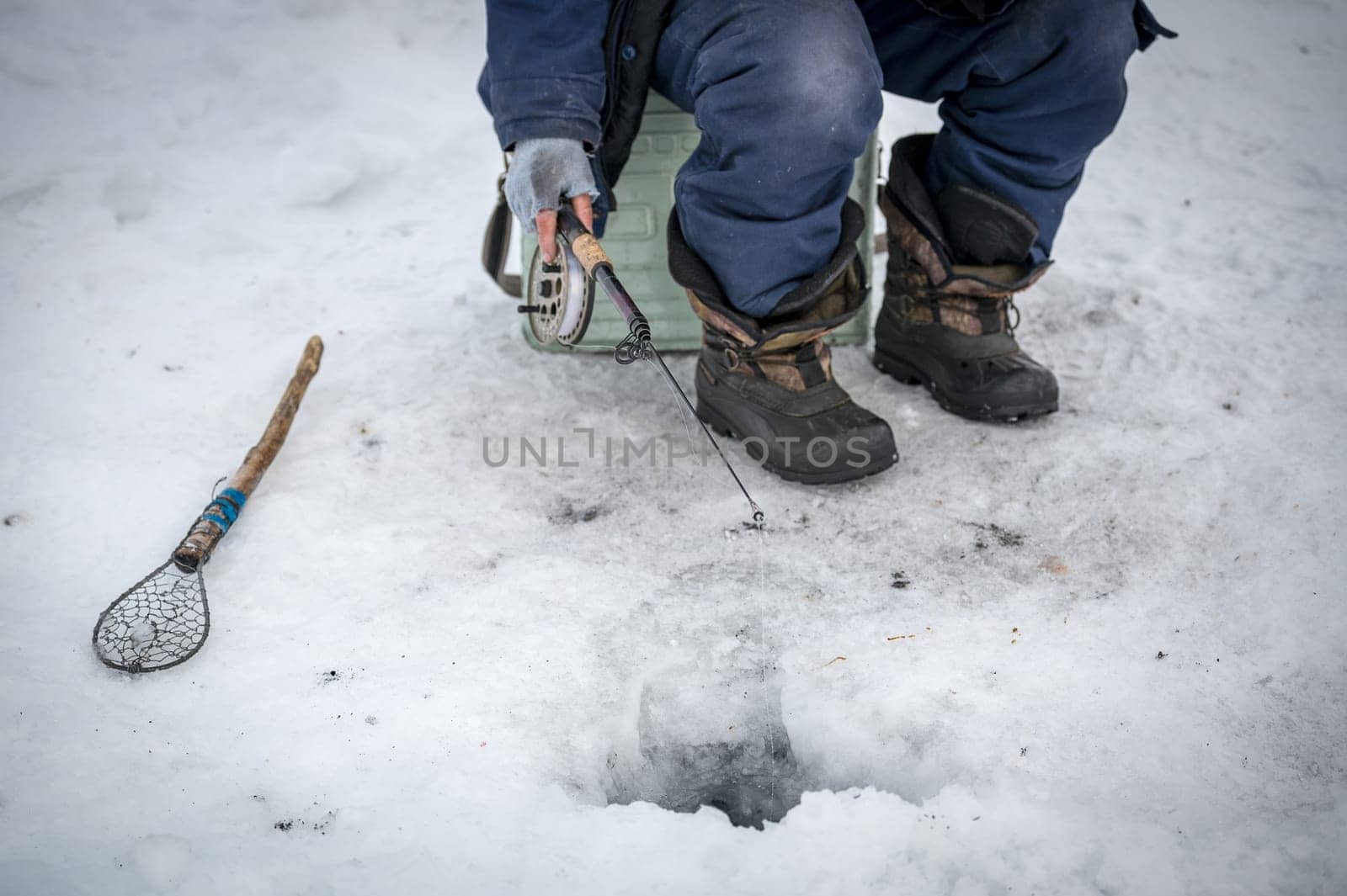 Baikal lake, Siberia, Russia - March 05, 2020 : Winter ice fishing. A fisherman is fishing on spinings near tents and cars on Lake Baikal on a March day. Baikal lake, Siberia, Russia