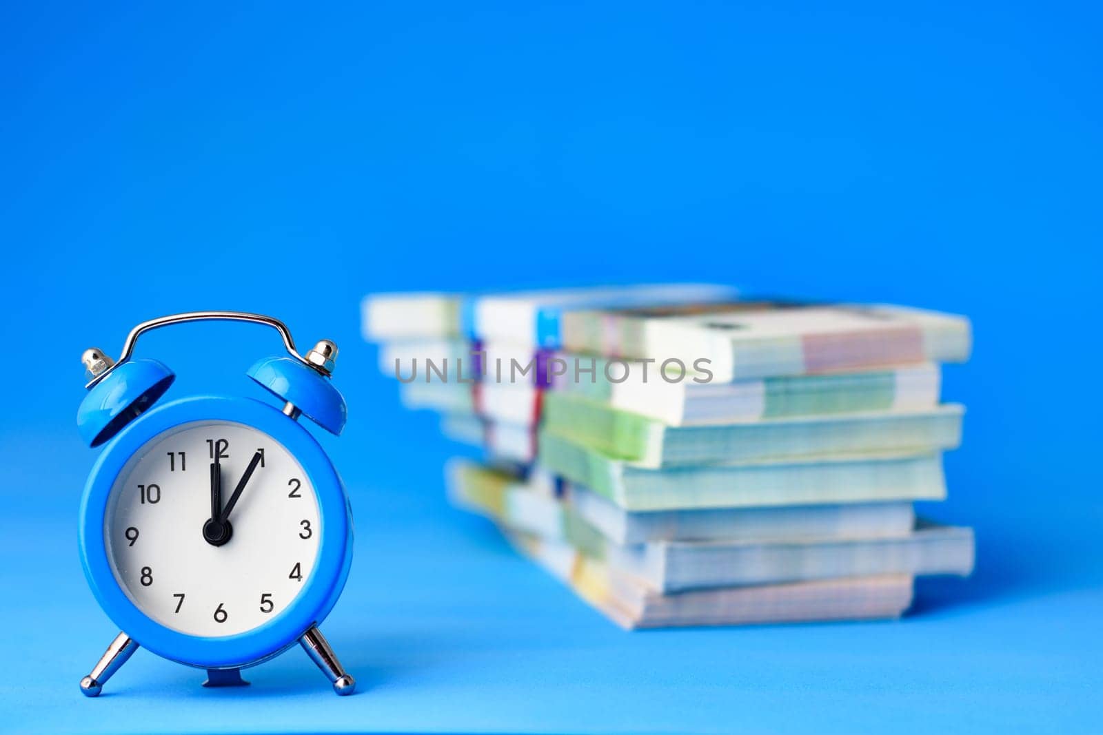 In the foreground is an alarm clock, in the background is a stack of bills