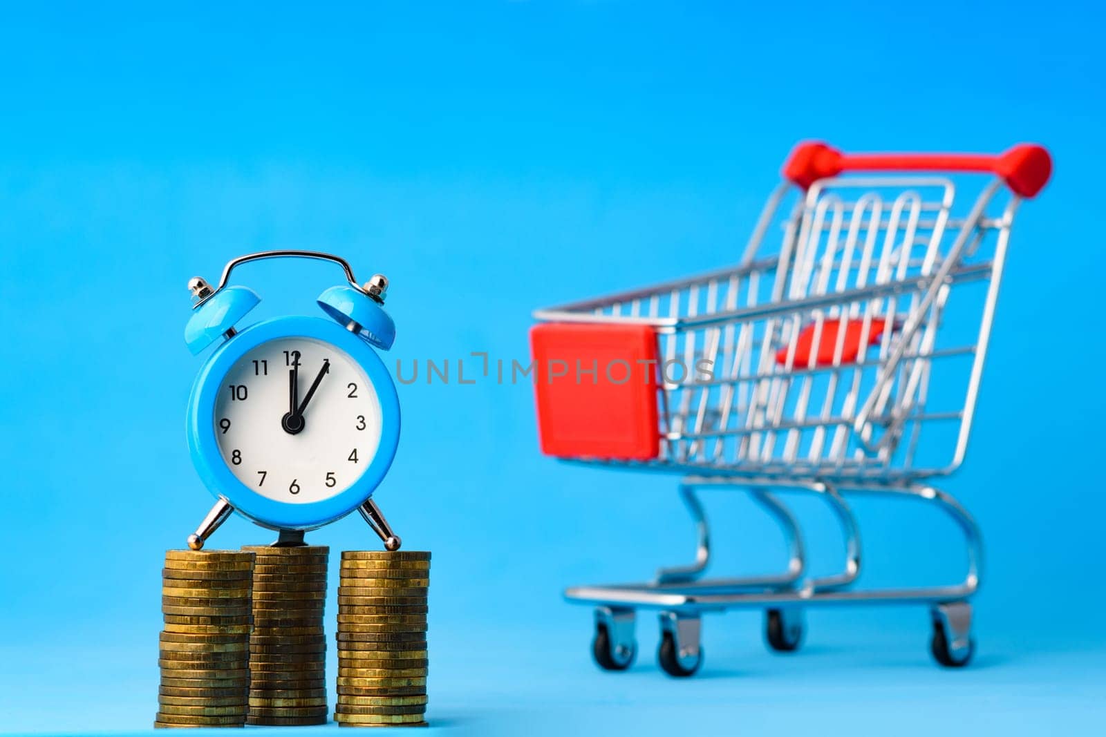 A clock stands on a stack of coins, in the background a grocery cart