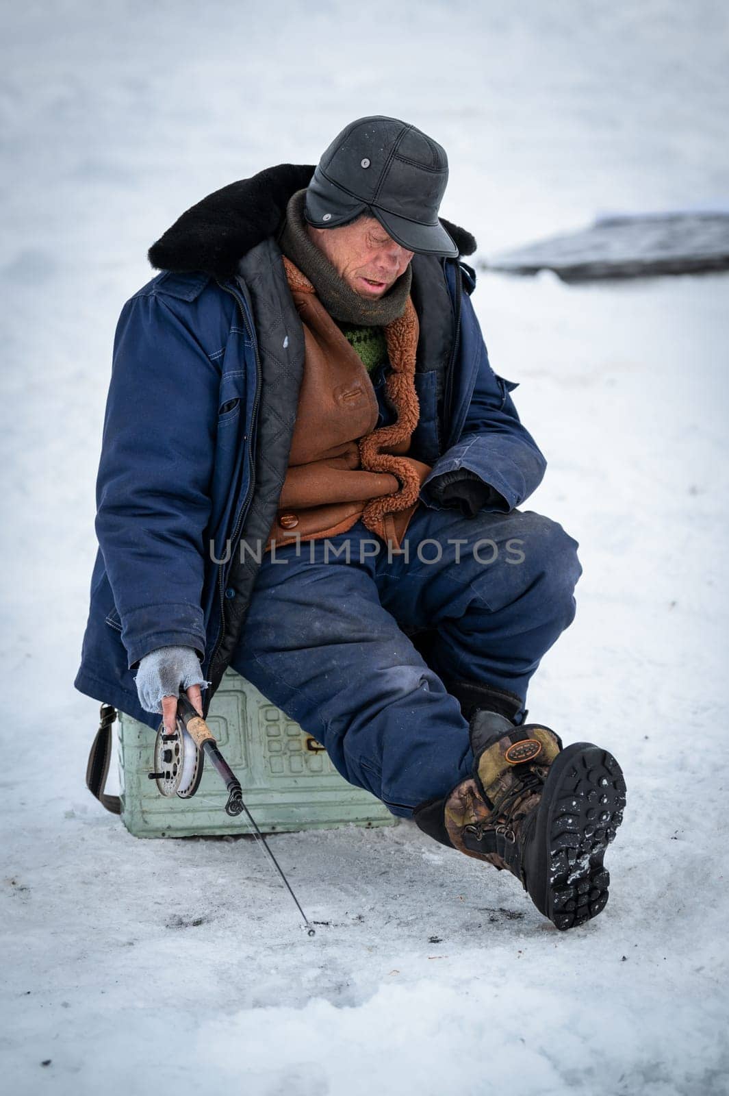 Baikal lake, Siberia, Russia - March 05, 2020 : Winter ice fishing. A fisherman is fishing on spinings near tents and cars on Lake Baikal on a March day. Baikal lake, Siberia, Russia