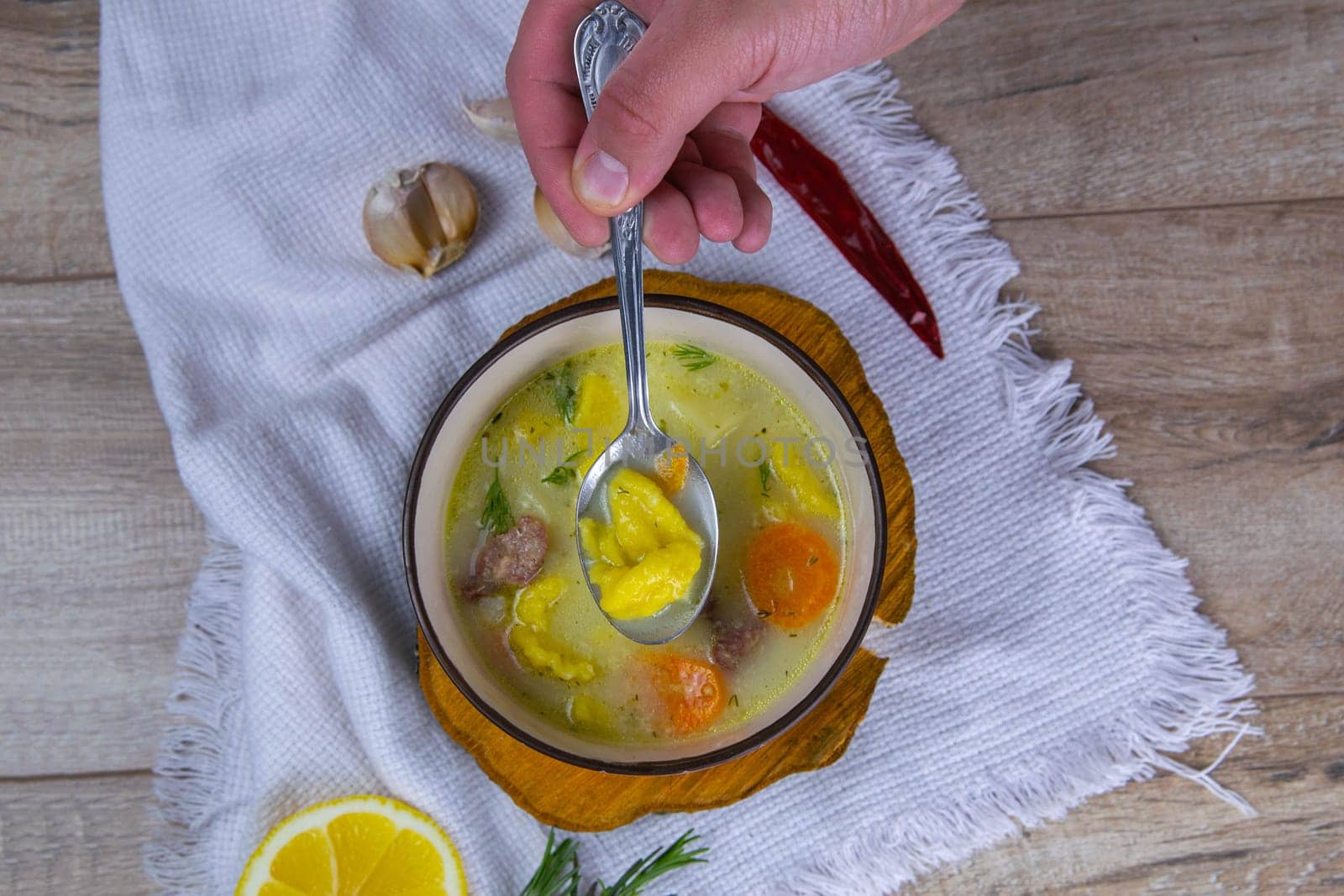 Hand takes a spoonful of soup .Potato cream soup with mushrooms, carrots and cheese. Top view. Soup in a brown plate, stands on a wooden stand, next to a hour, spoon, spices and lemon.