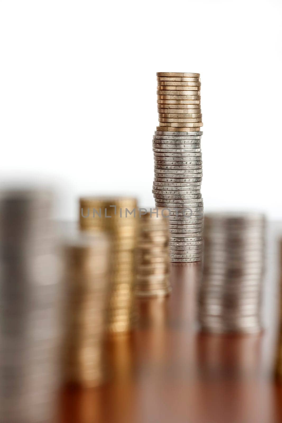 Flat-angled view of stacked euro coins on smooth wooden background. Focus on the last stack with aperture F8.