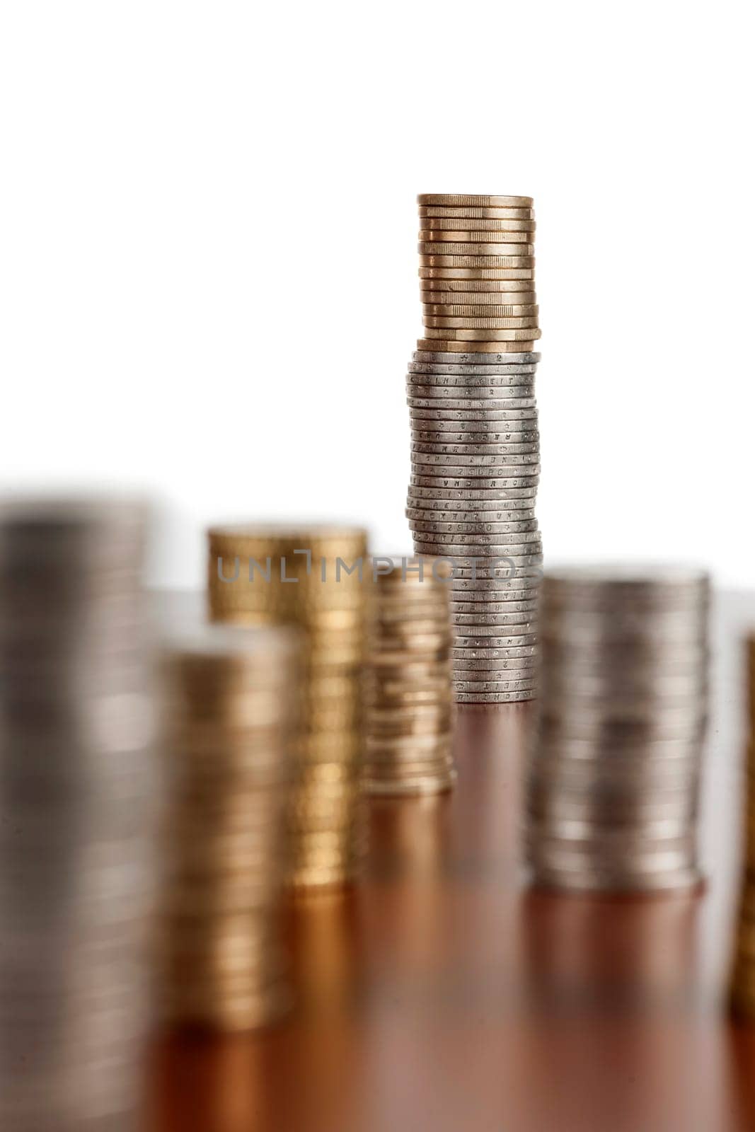 Flat-angled view of stacked euro coins on smooth wooden surface and focus on the rear stack with aperture F11.
