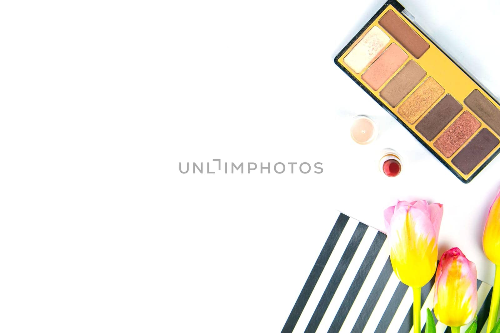 Tulips with green women's clutch, pallet with shadows and women's cosmetics on a white background.